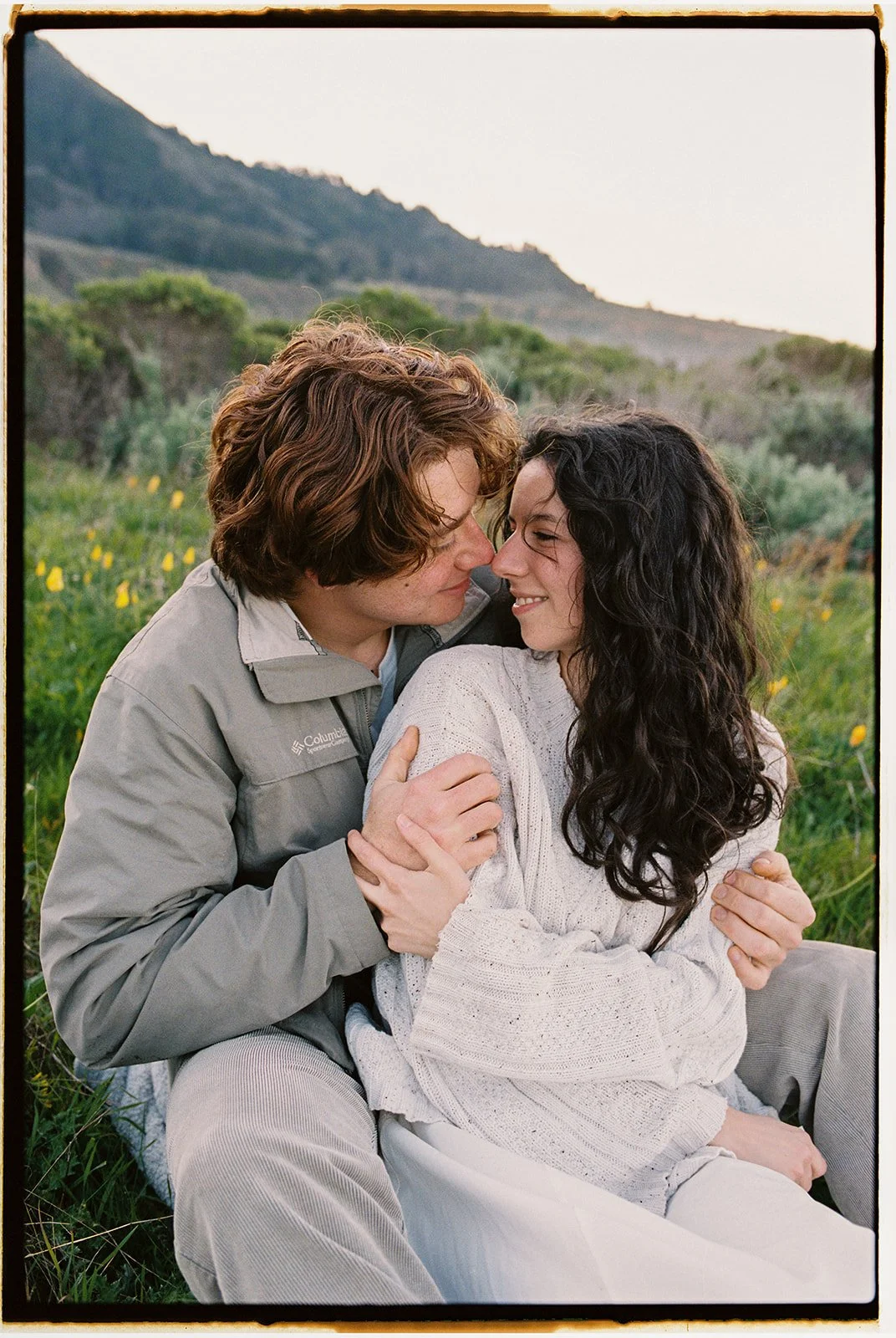 film photo of a man and woman taking engagement photos together in a grassy field