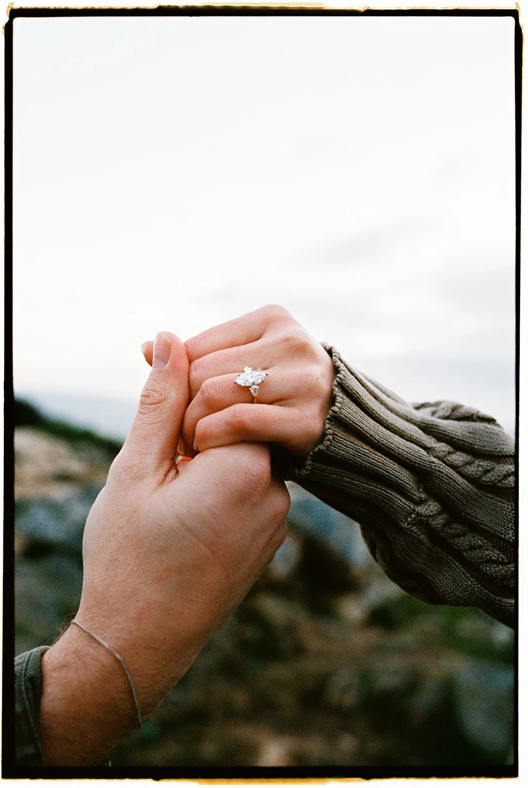 a close up photo taken on film of a couple holding hands with an engagement ring being shown