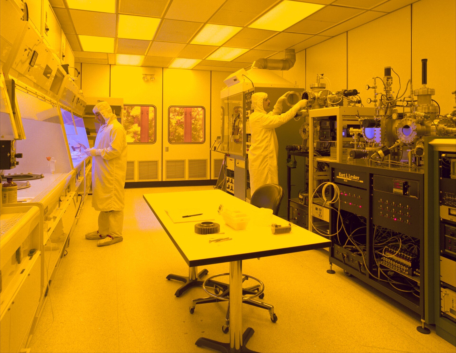 Technicians in protective suits working with laboratory equipment inside a microchip clean room.