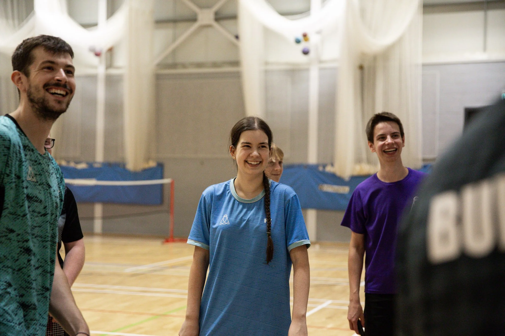 Group of young adults smiling and laughing in a gymnasium, wearing sports jerseys and casual sportswear.