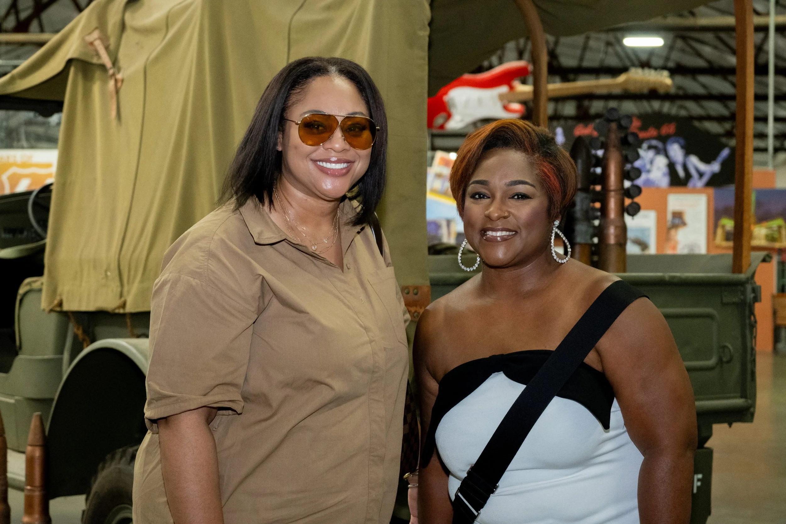 Two women smile for a photo beside a vintage vehicle at the event.