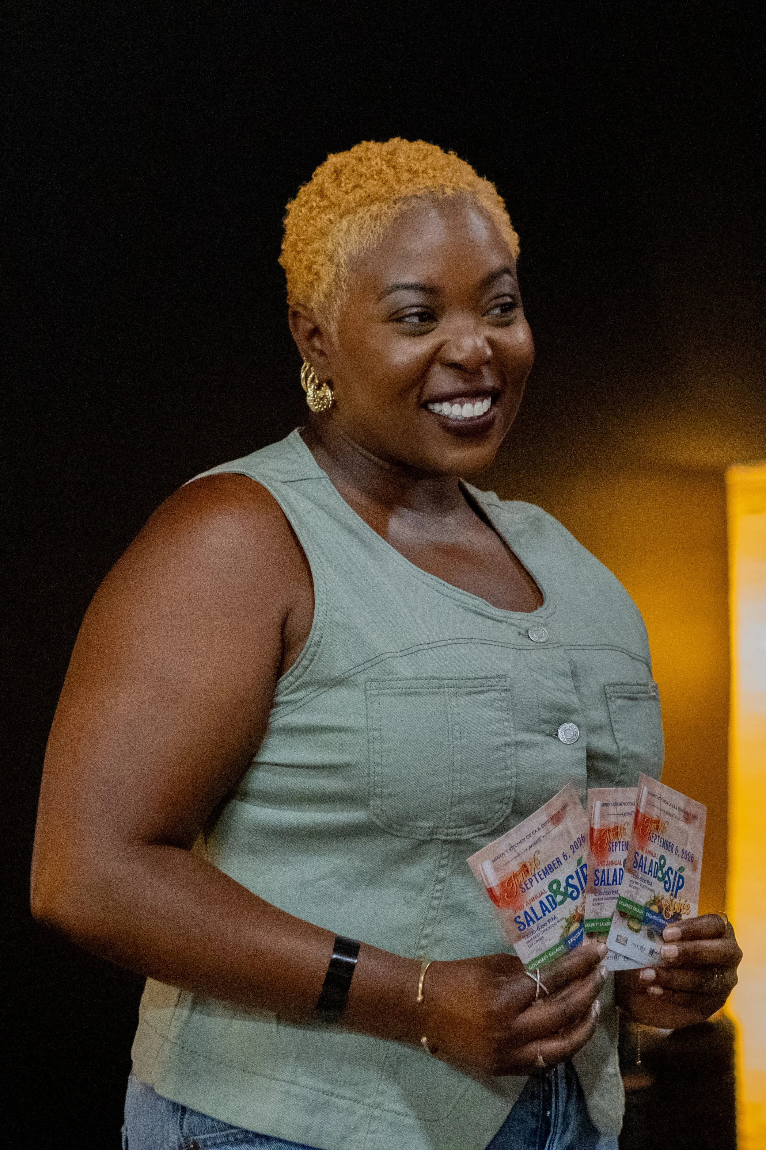 A smiling woman holds promotional flyers for a salad and wine event.