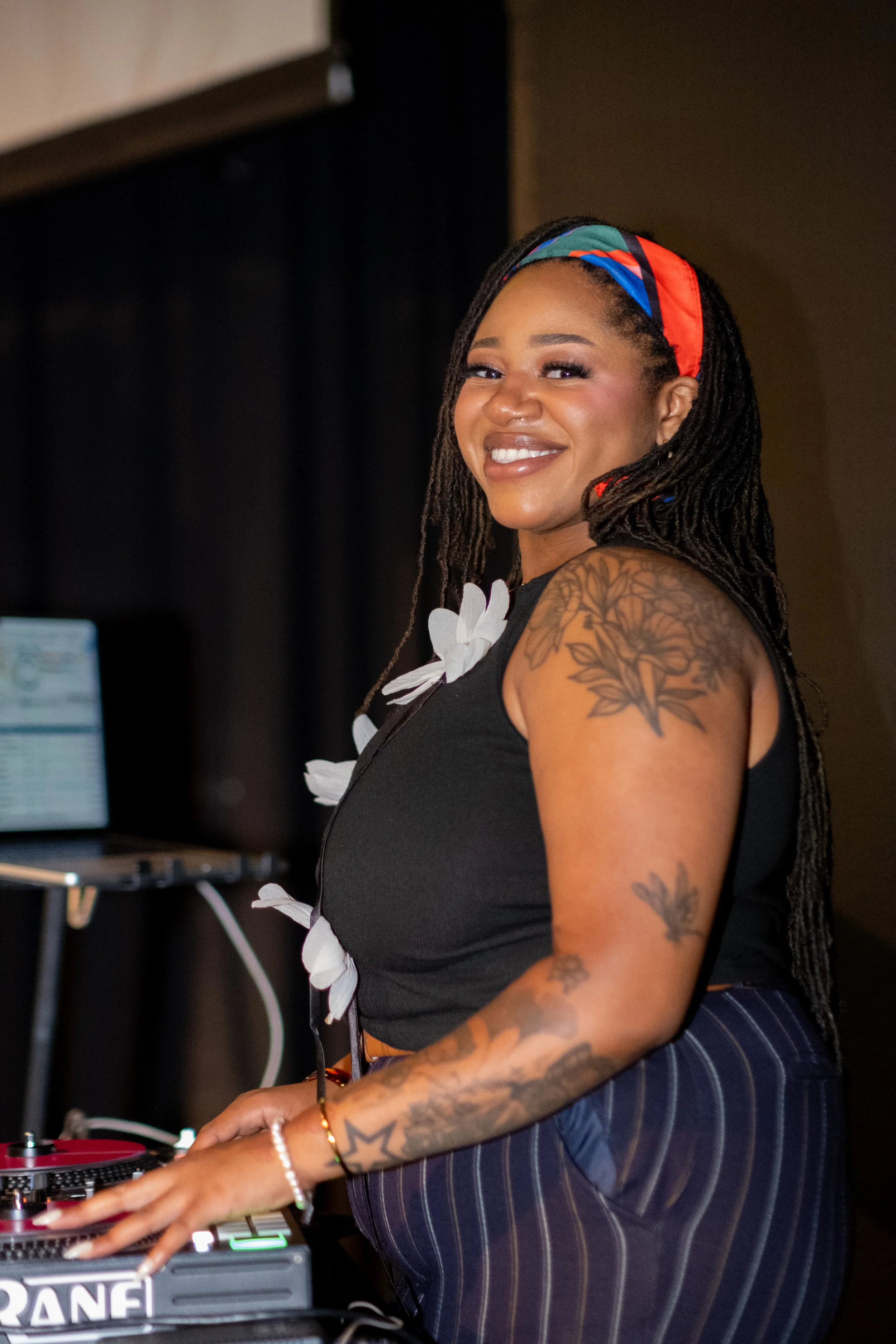 A smiling woman with long braids operates a DJ turntable.