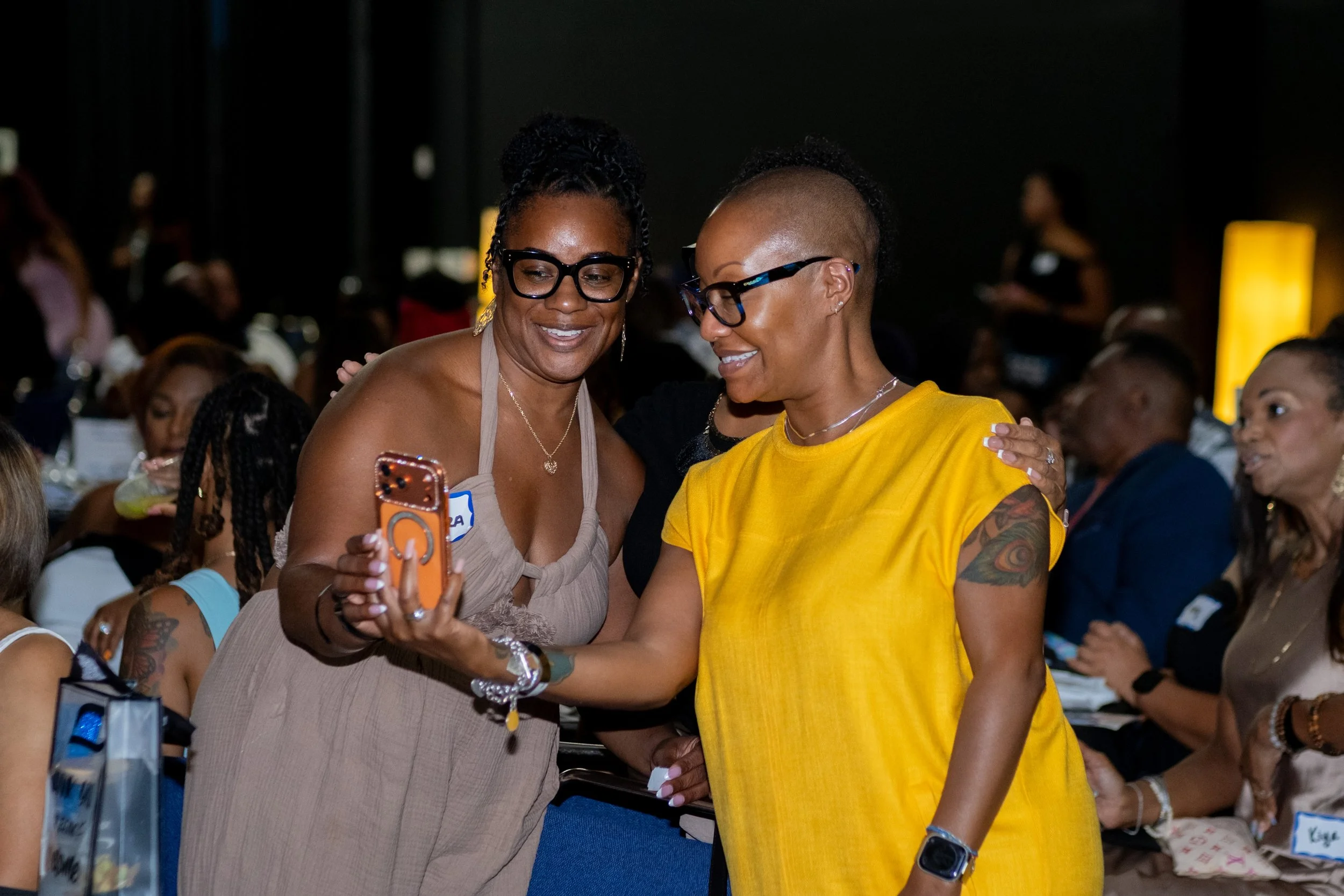 Two women smile together while taking a selfie during the event.