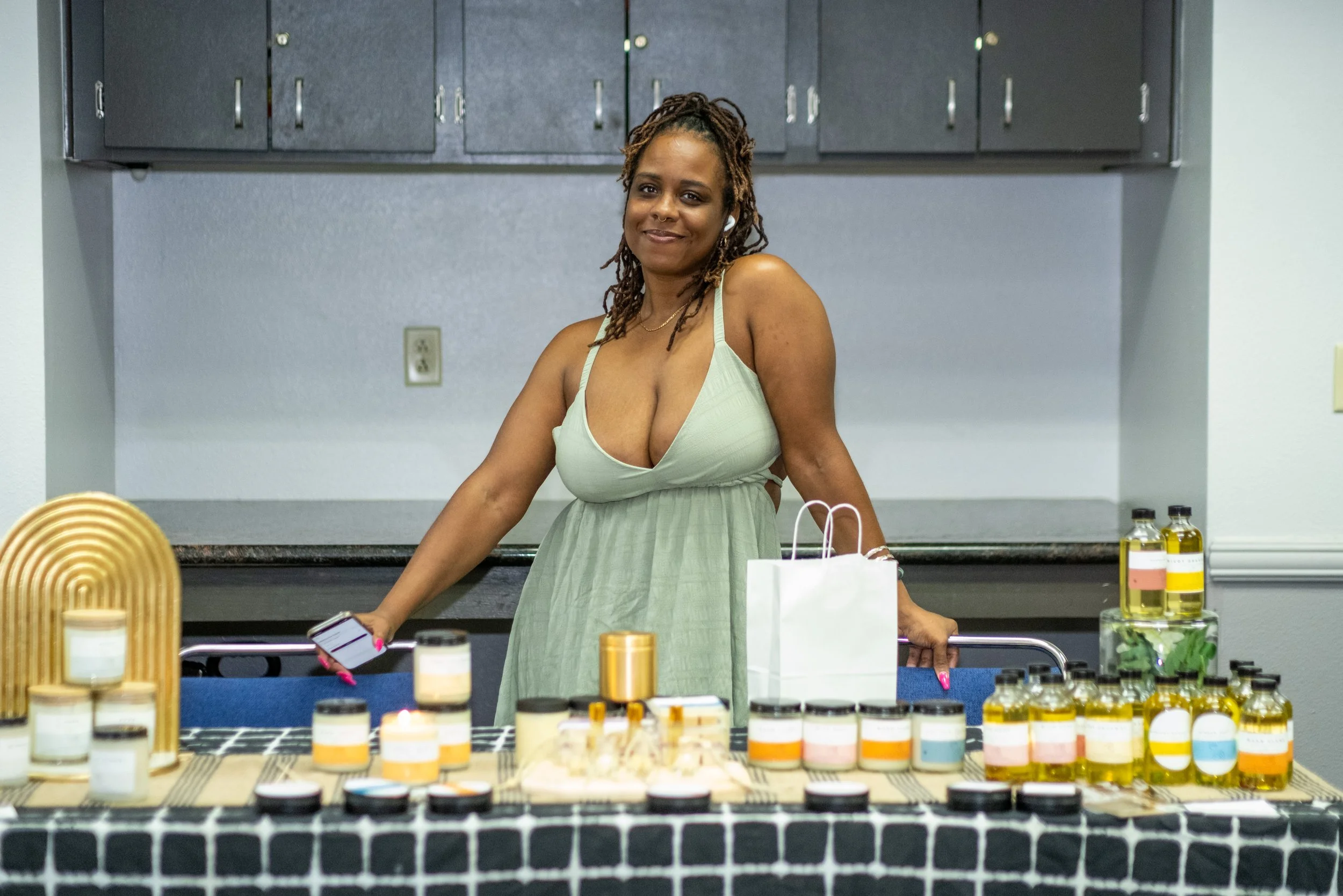 A vendor stands behind a table displaying candles, oils, and other products.