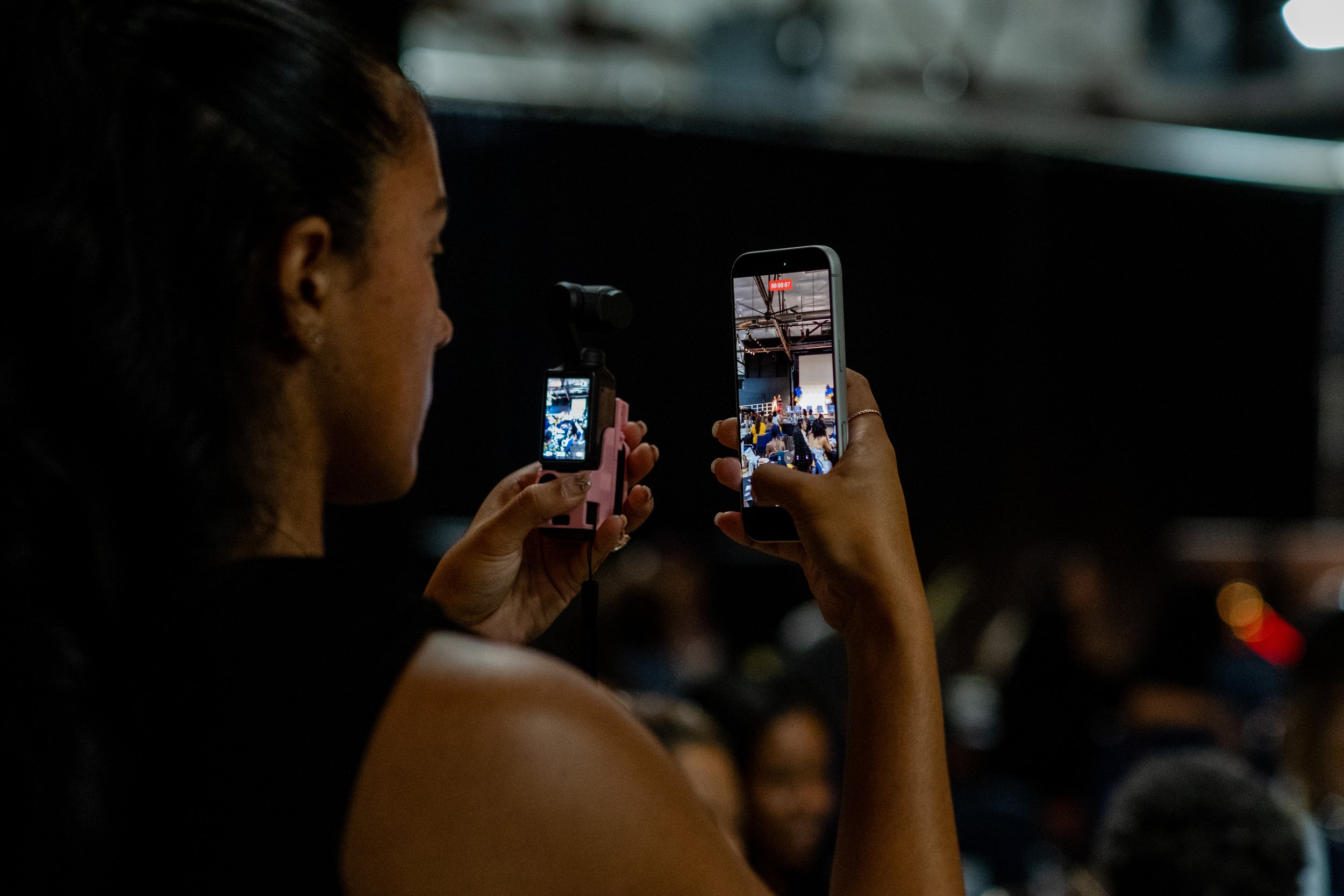 An attendee records the event with two smartphones while seated in the audience.