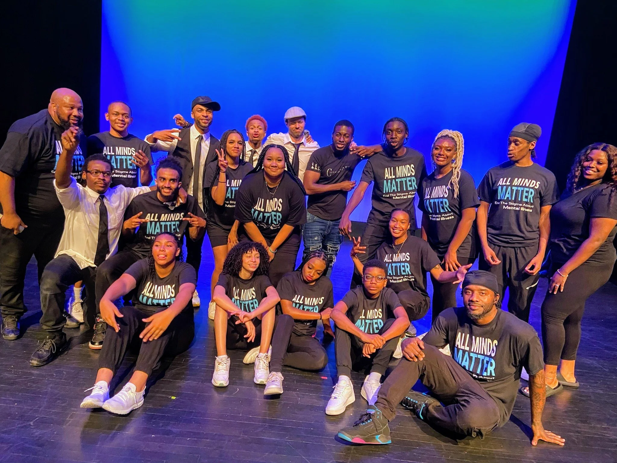 Group of diverse people on stage, some wearing matching black t-shirts with