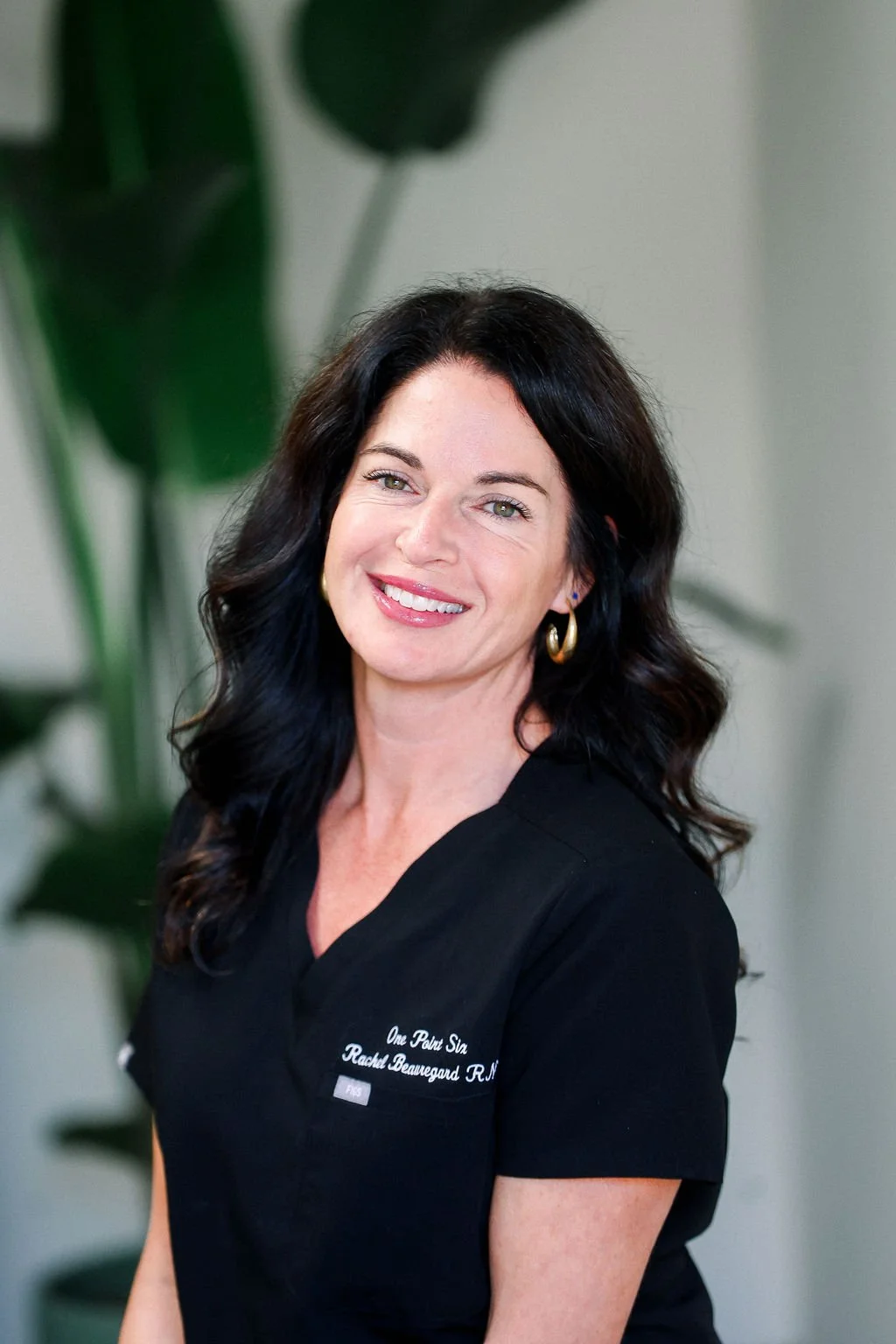 A woman with long black hair, wearing a black shirt with white embroidery, smiling indoors.