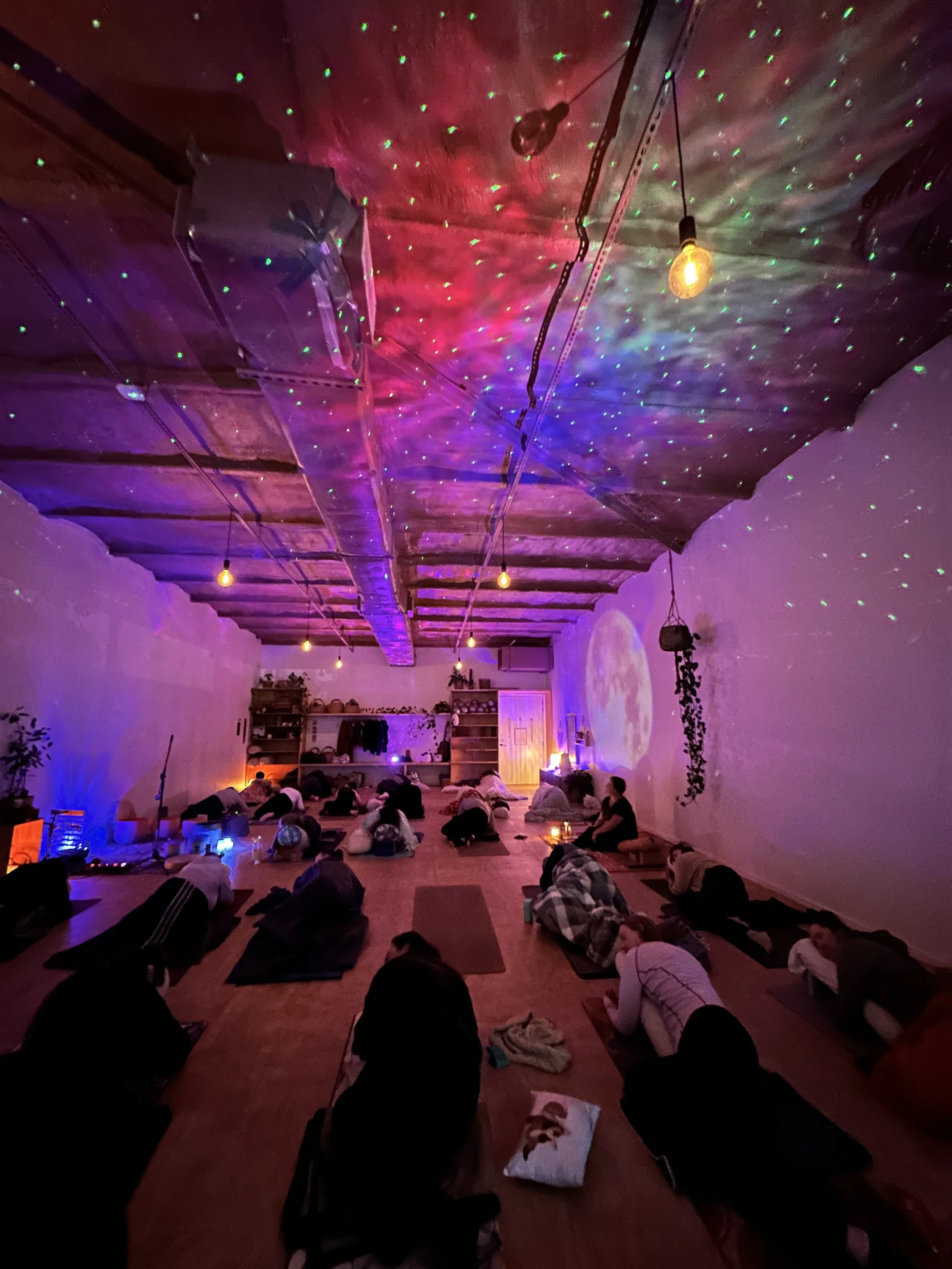 People practicing yoga in a dimly lit studio with colorful star-shaped light projections on the ceiling, creating a peaceful atmosphere.