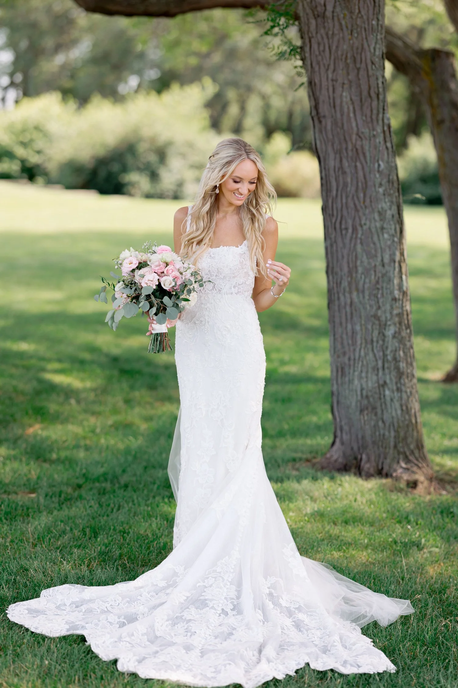 The bride poses elegantly in the Art Institute South Gardens, her lace gown and blush bouquet radiant against the soft green lawn and tall oak tree behind her.