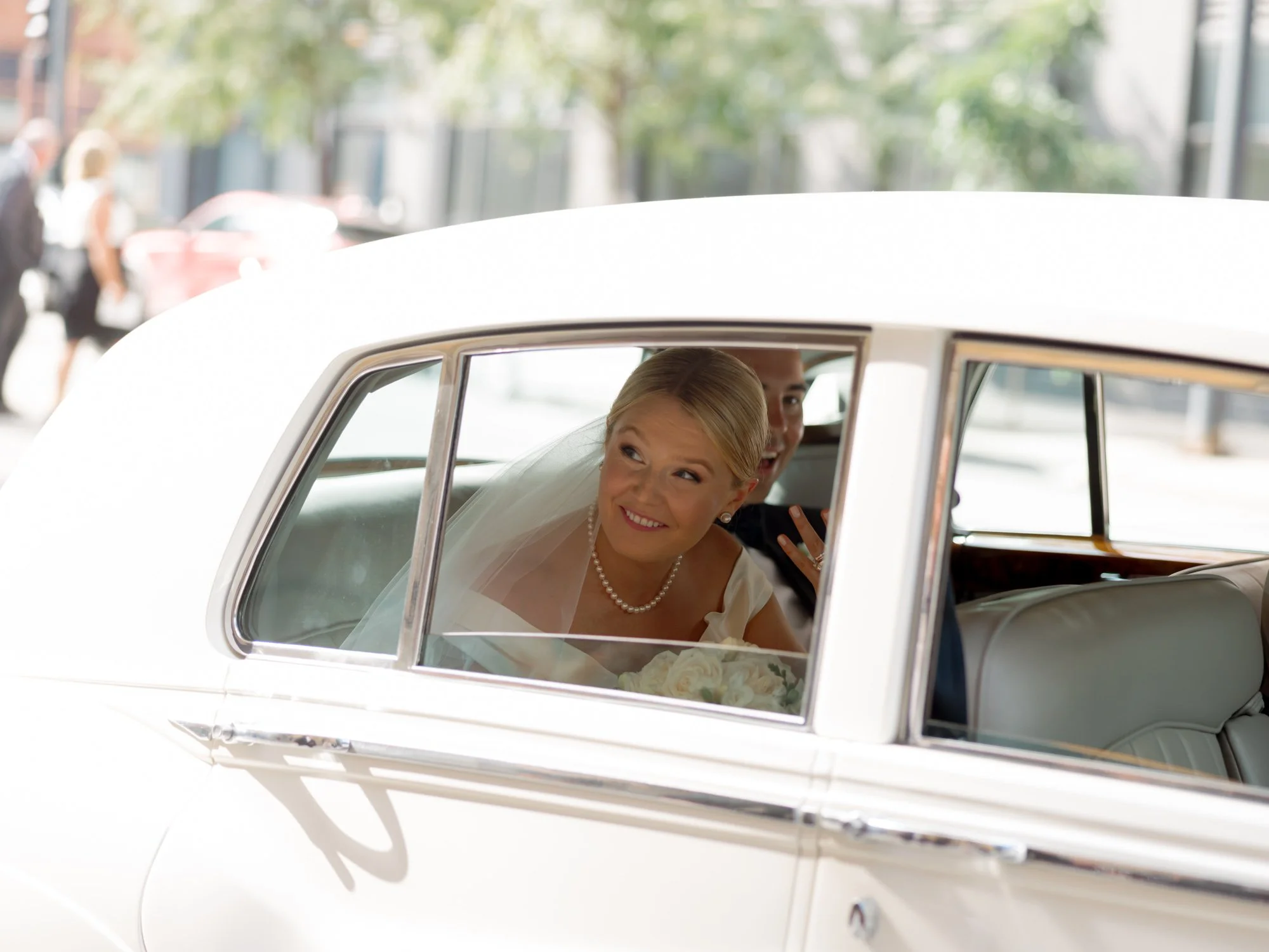 The bride gazes out the vintage Rolls-Royce window with a soft smile, her cathedral veil catching the afternoon light on the ride to the Union League Club.