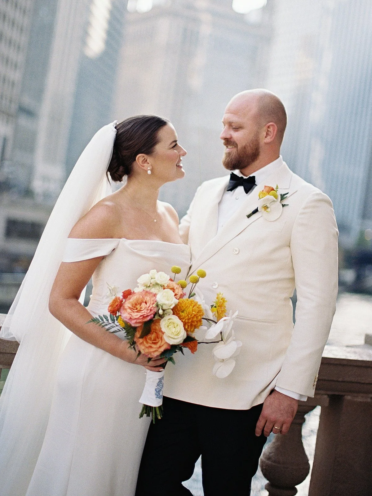 Bride and groom laughing face-to-face on the Chicago Riverwalk bridge, the city skyline soft and golden behind them — a purely candid, joyful film portrait.
