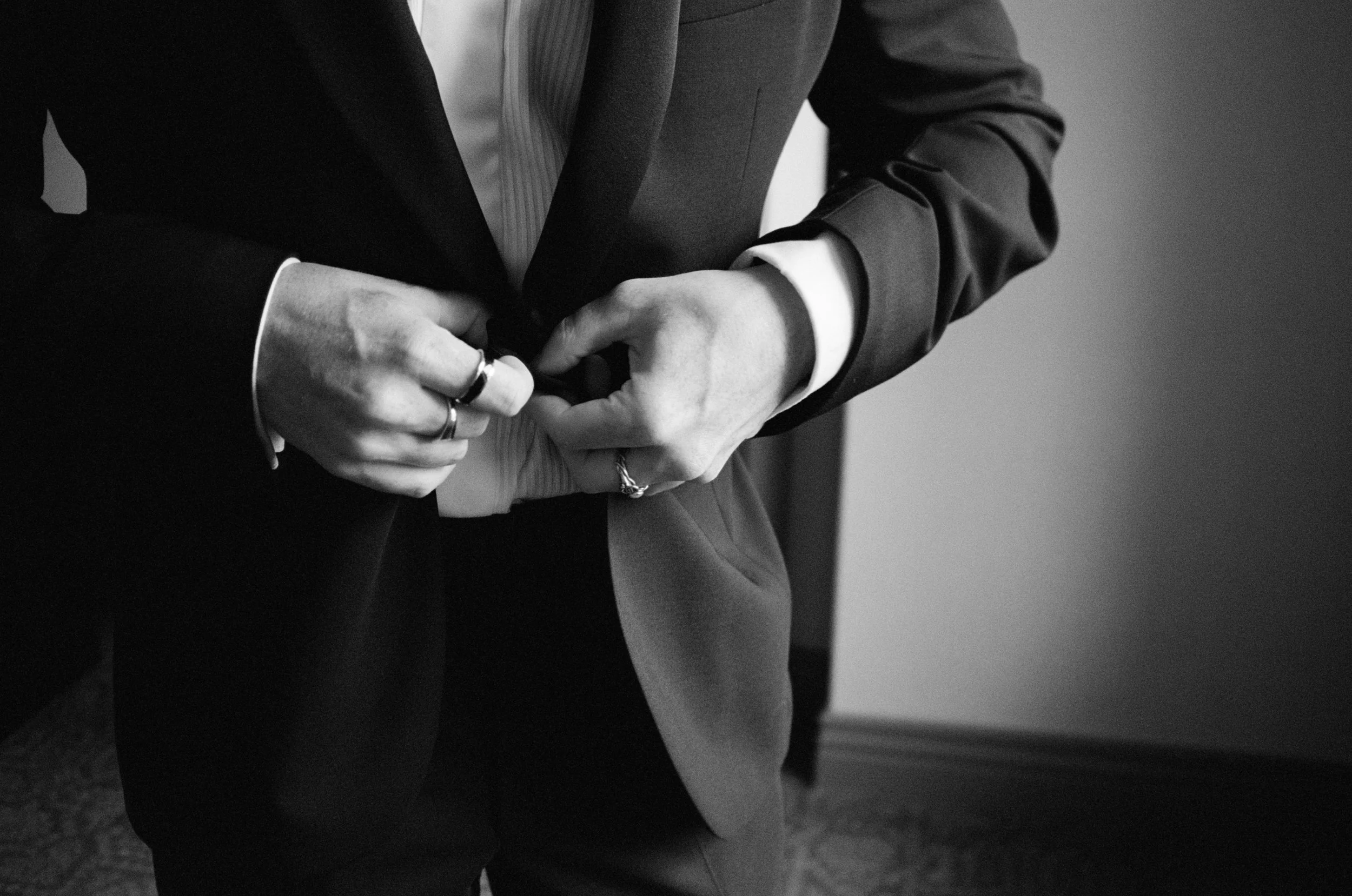 Black and white close-up of the groom buttoning his tuxedo jacket