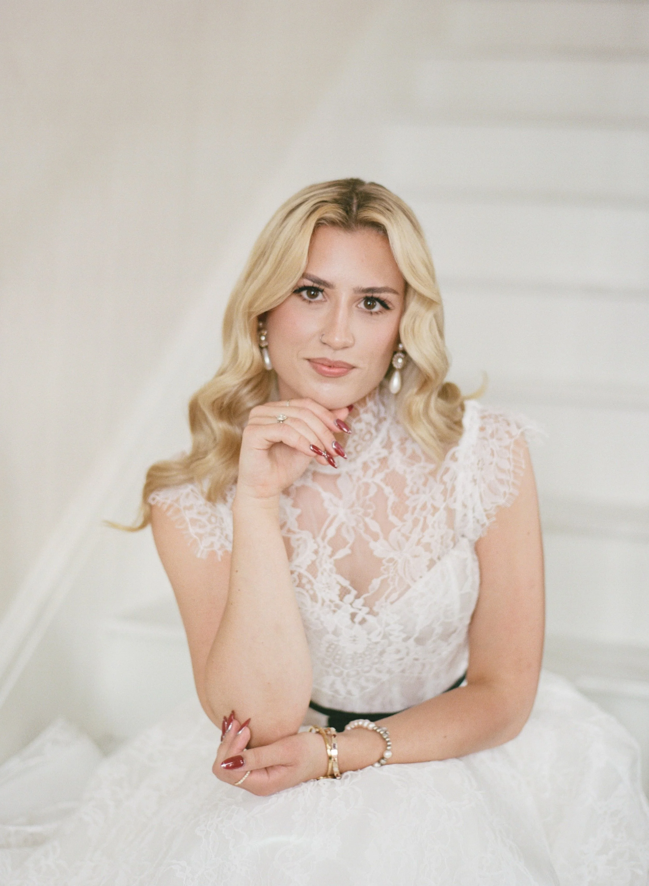 Editorial bridal portrait on a white staircase, hand resting thoughtfully on her chin