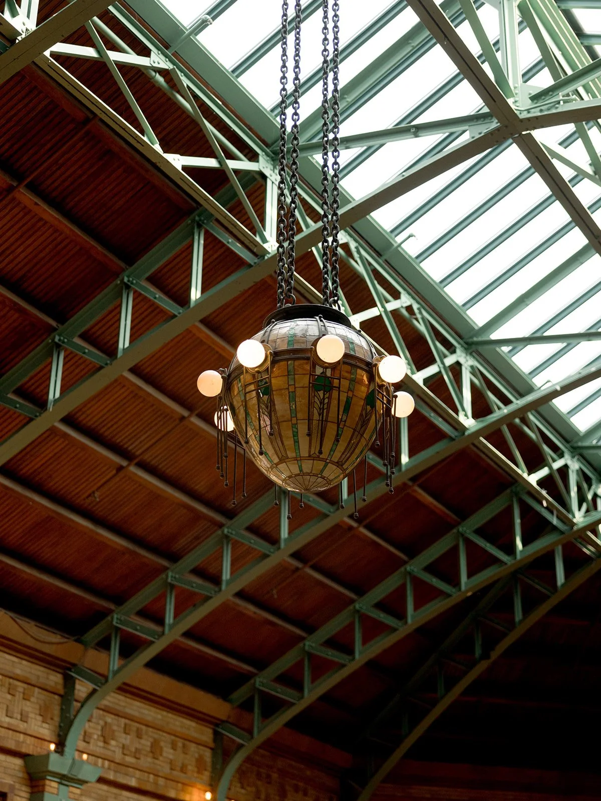 One of Cafe Brauer's original antique chandeliers against the Great Hall's soaring green steel trusses and wood ceiling.