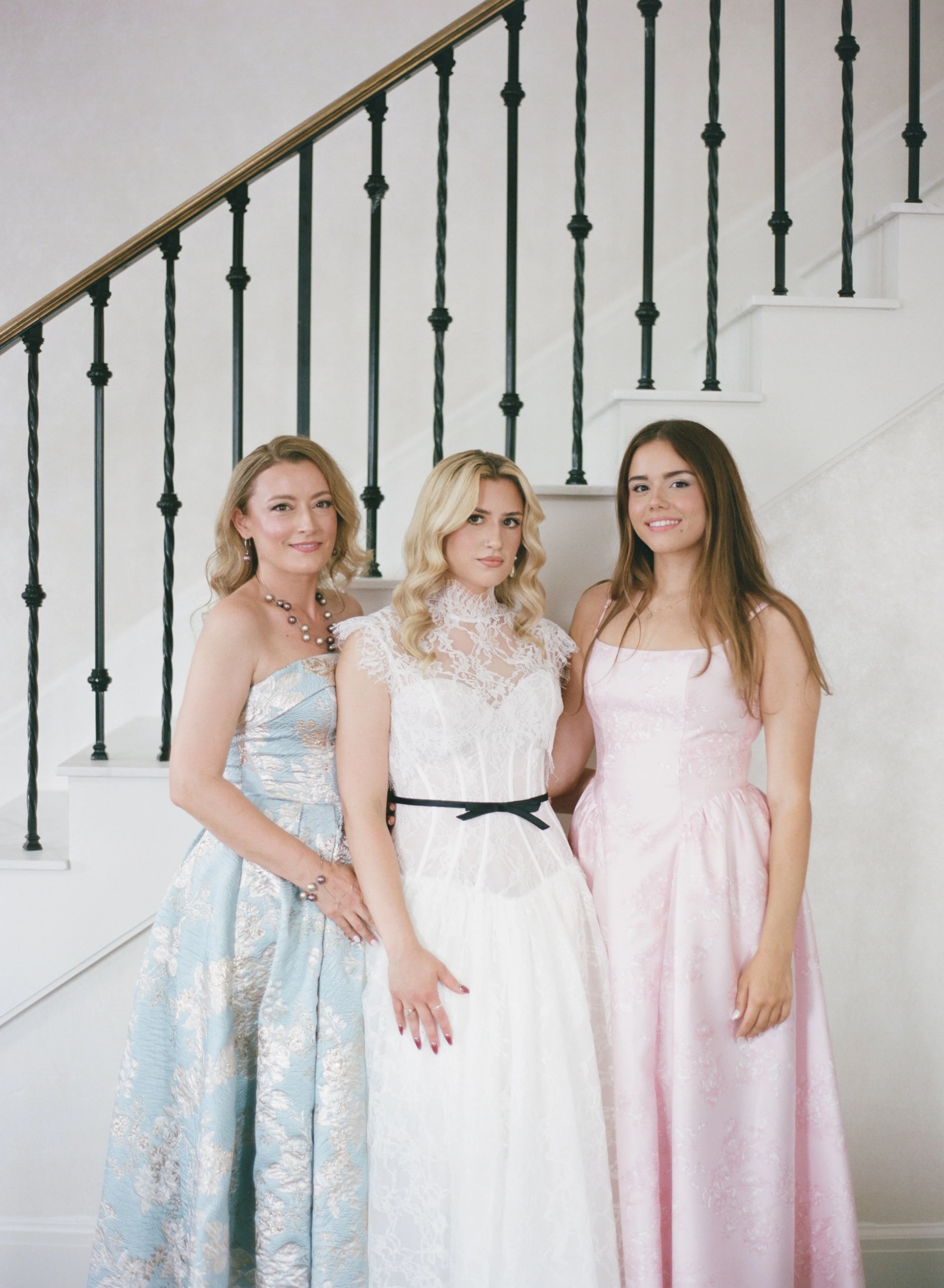 Three bridesmaids in pastel gowns pose together on a staircase