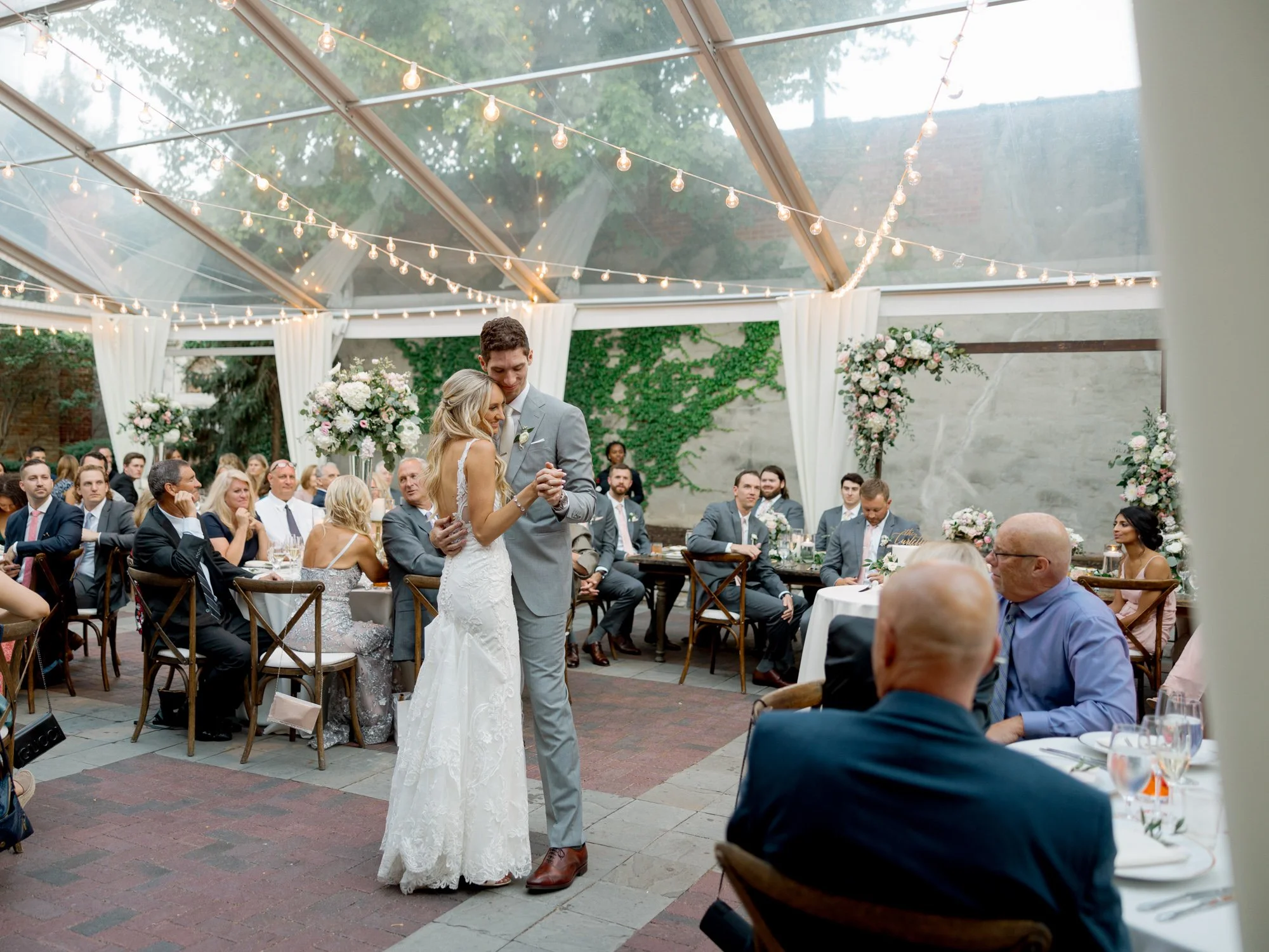 The bride and groom share their first dance under the Chicago Illuminating Company's glass tent, surrounded by candlelit tables and adoring guests.