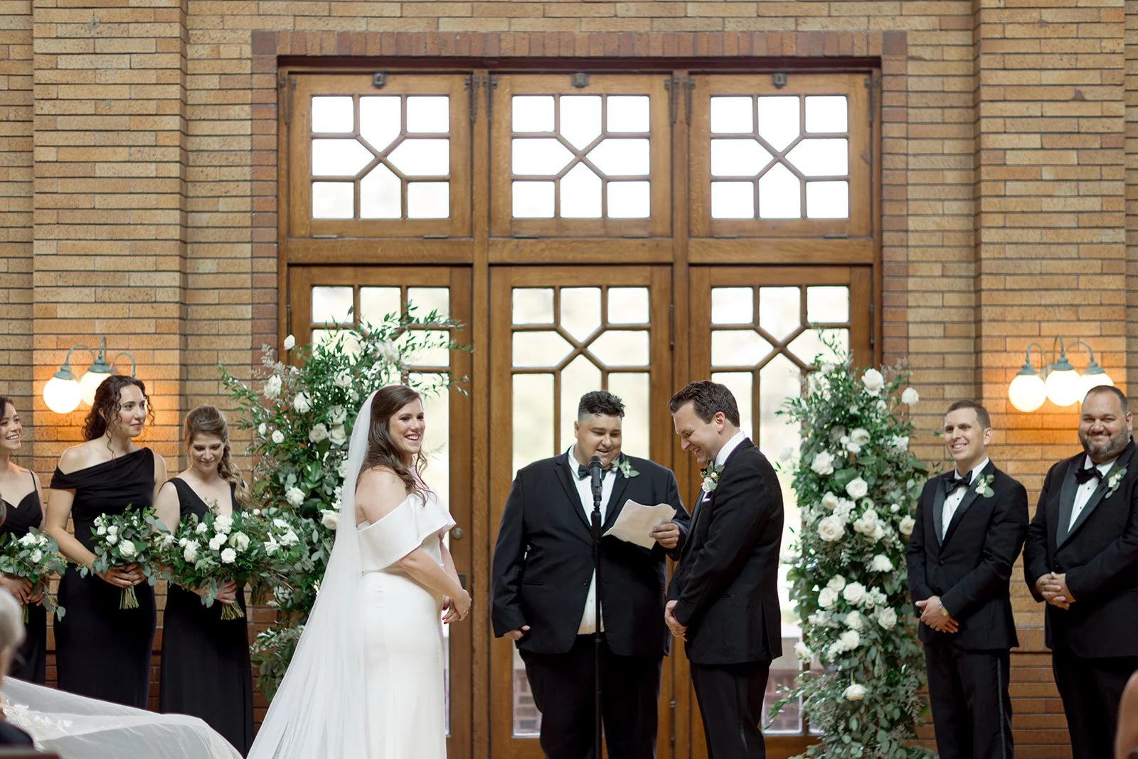 Bride and groom at the altar of Cafe Brauer's Great Hall with their officiant and twin white floral arches.