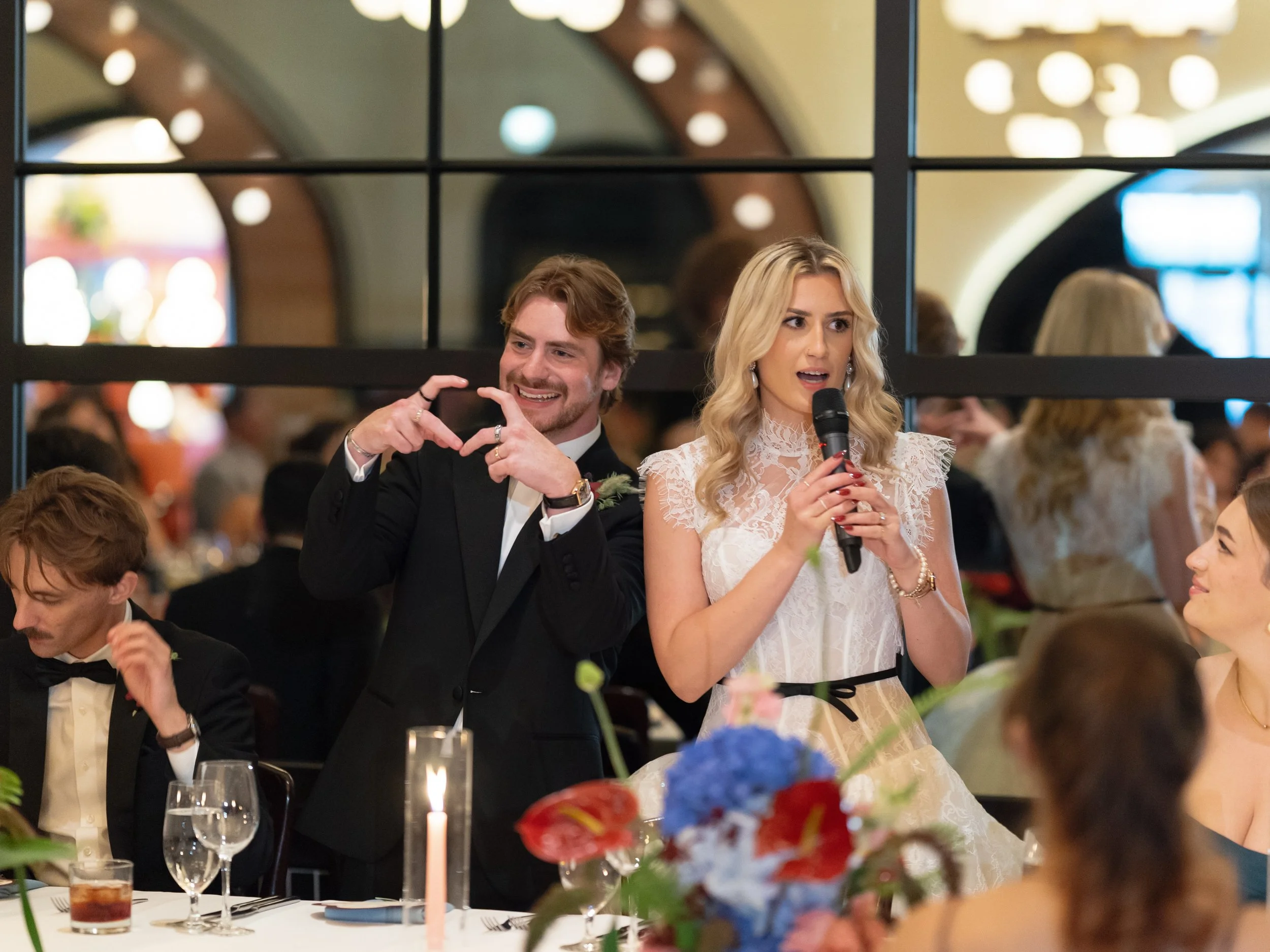 Bride and groom make heart shapes with their hands during a reception toast