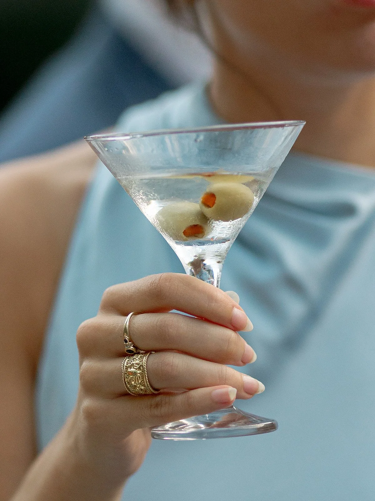 Close-up of a wedding guest holding a dirty martini with gold rings on her fingers during cocktail hour at Community House Winnetka, photographed by Chicago film wedding photographer Louie Abellera.