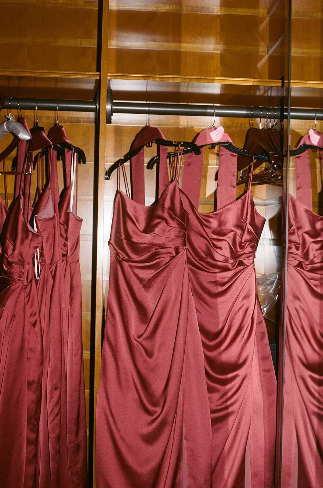 Bridesmaids' burgundy satin gowns hanging on an ornate gold-framed mirror in the getting ready suite at Chicago Athletic Association. Shot on film by a Chicago wedding photographer.