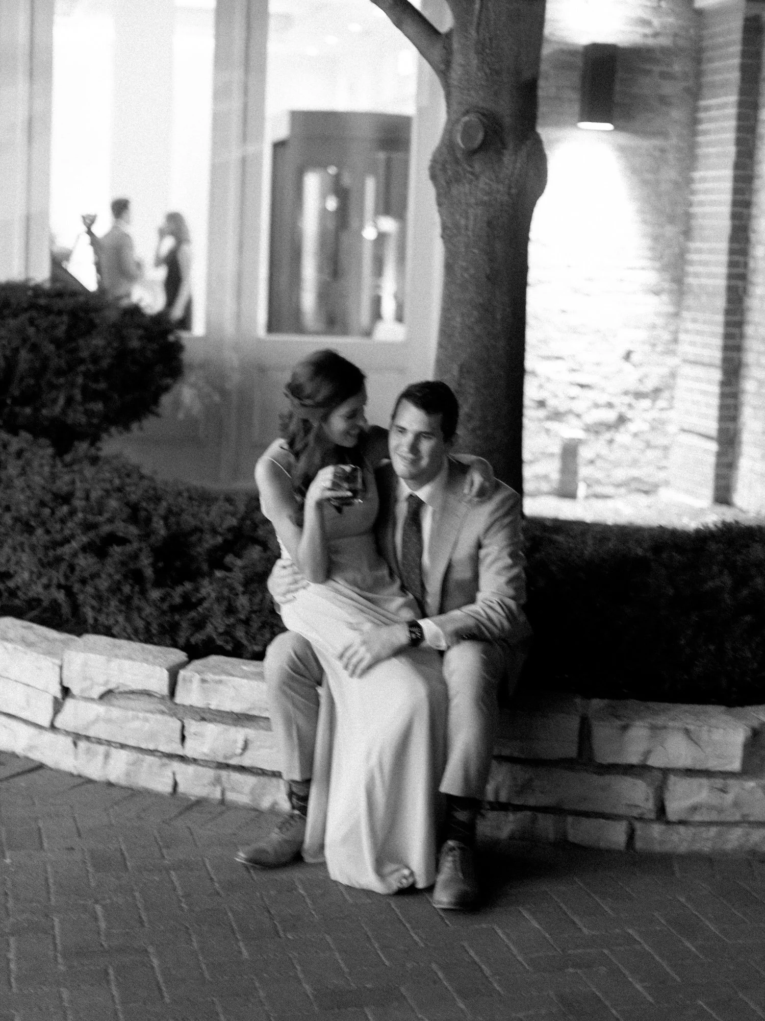 A moody black-and-white portrait of a couple sitting together on a stone ledge outside the Chicago Illuminating Company in the evening, relaxed and close.