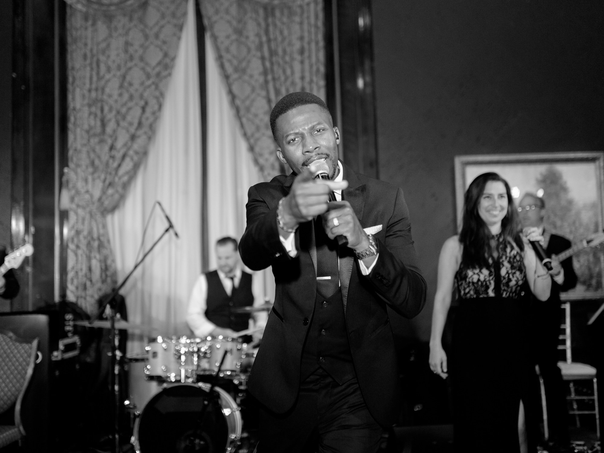 The band’s lead vocalist commands the microphone in black and white, pointing to the crowd — the kind of performer who keeps a dance floor going all night.
