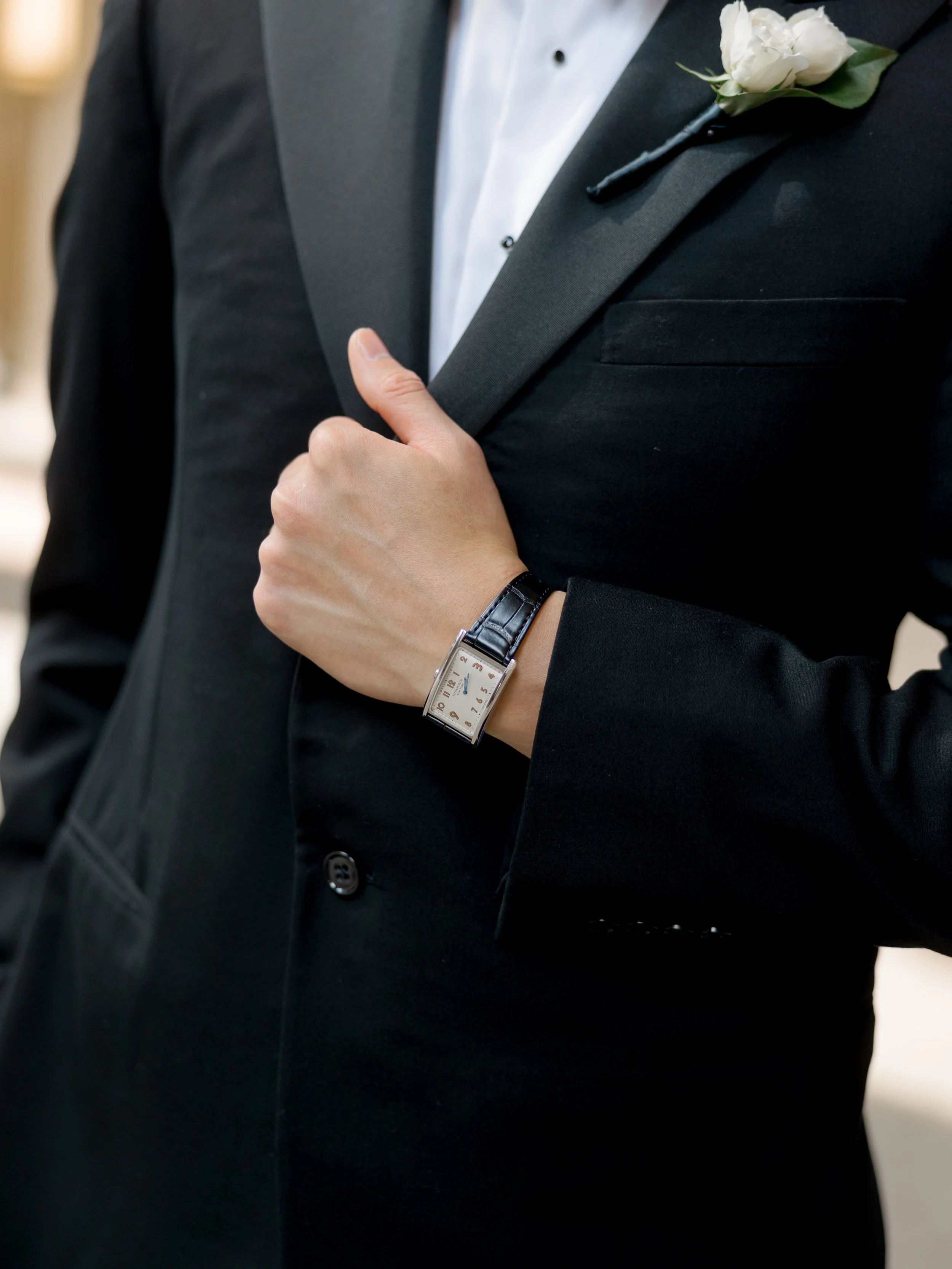 Close up of the grooms leather strap watch and white rose boutonniere on a black tuxedo at The Peninsula Chicago
