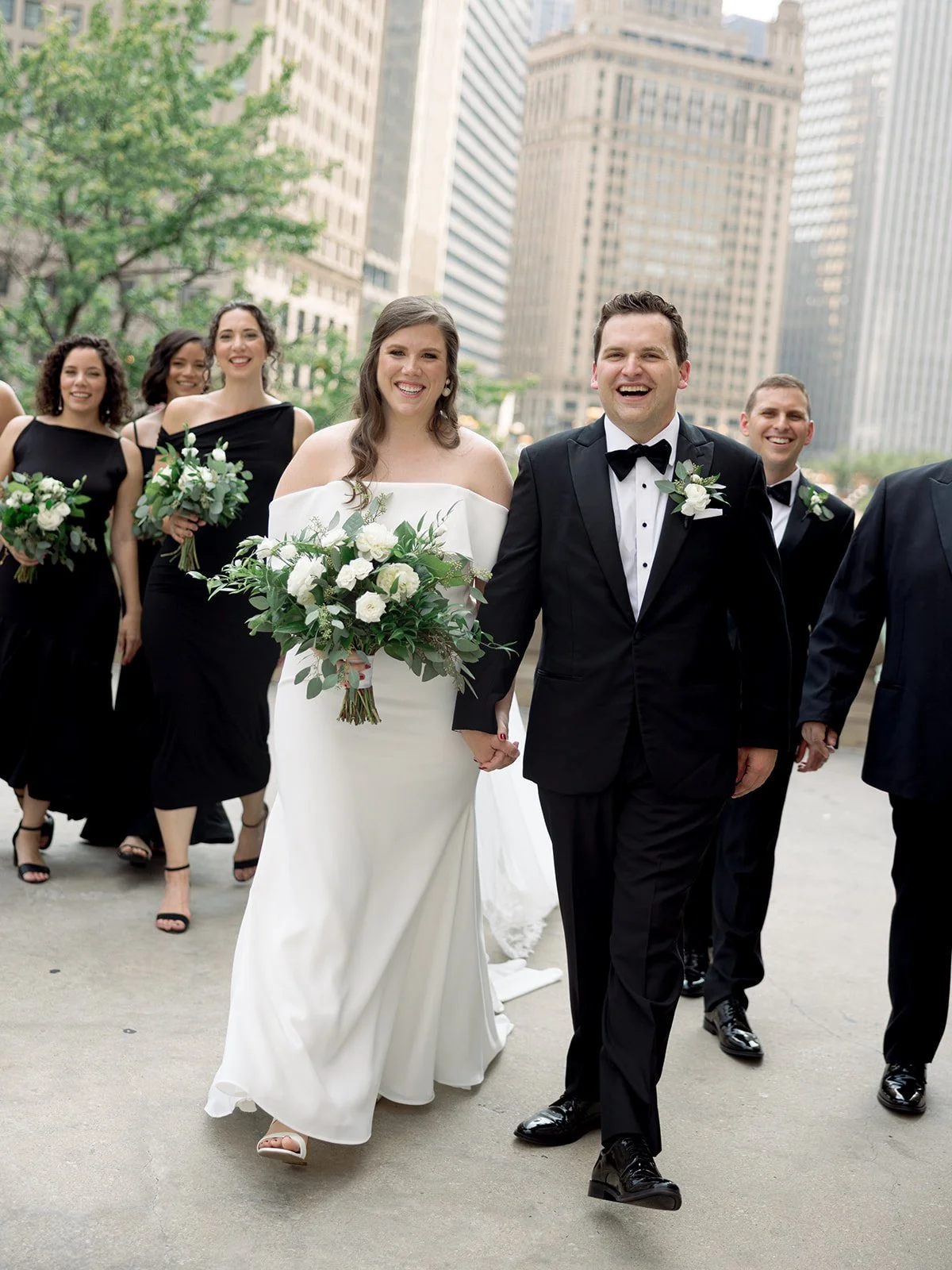 Bride and groom leading their wedding party in a joyful walk along the Chicago Riverwalk, laughing hand in hand.