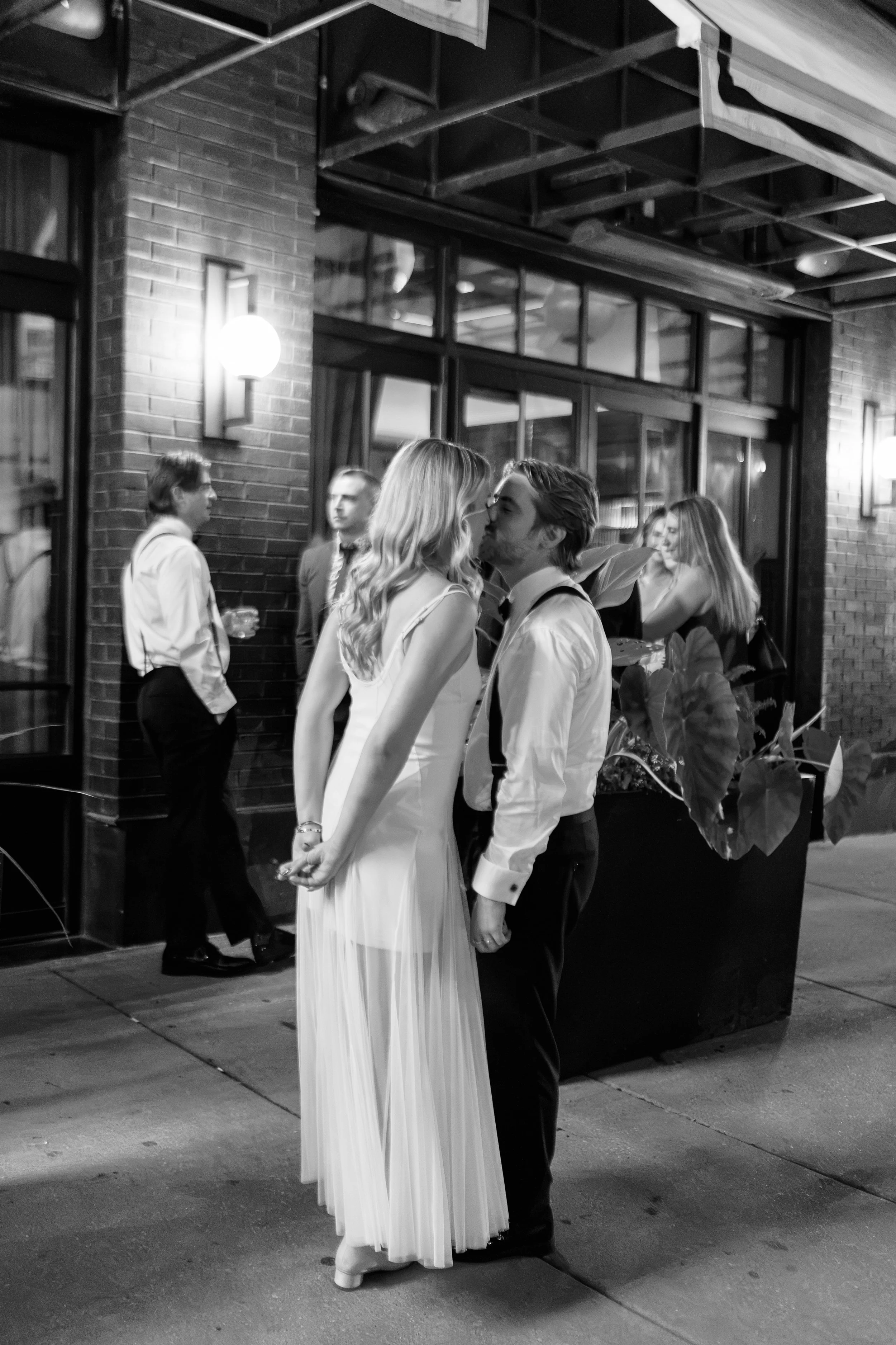 Black and white photo of the newlyweds sharing a kiss on the sidewalk outside The Wellsley at night