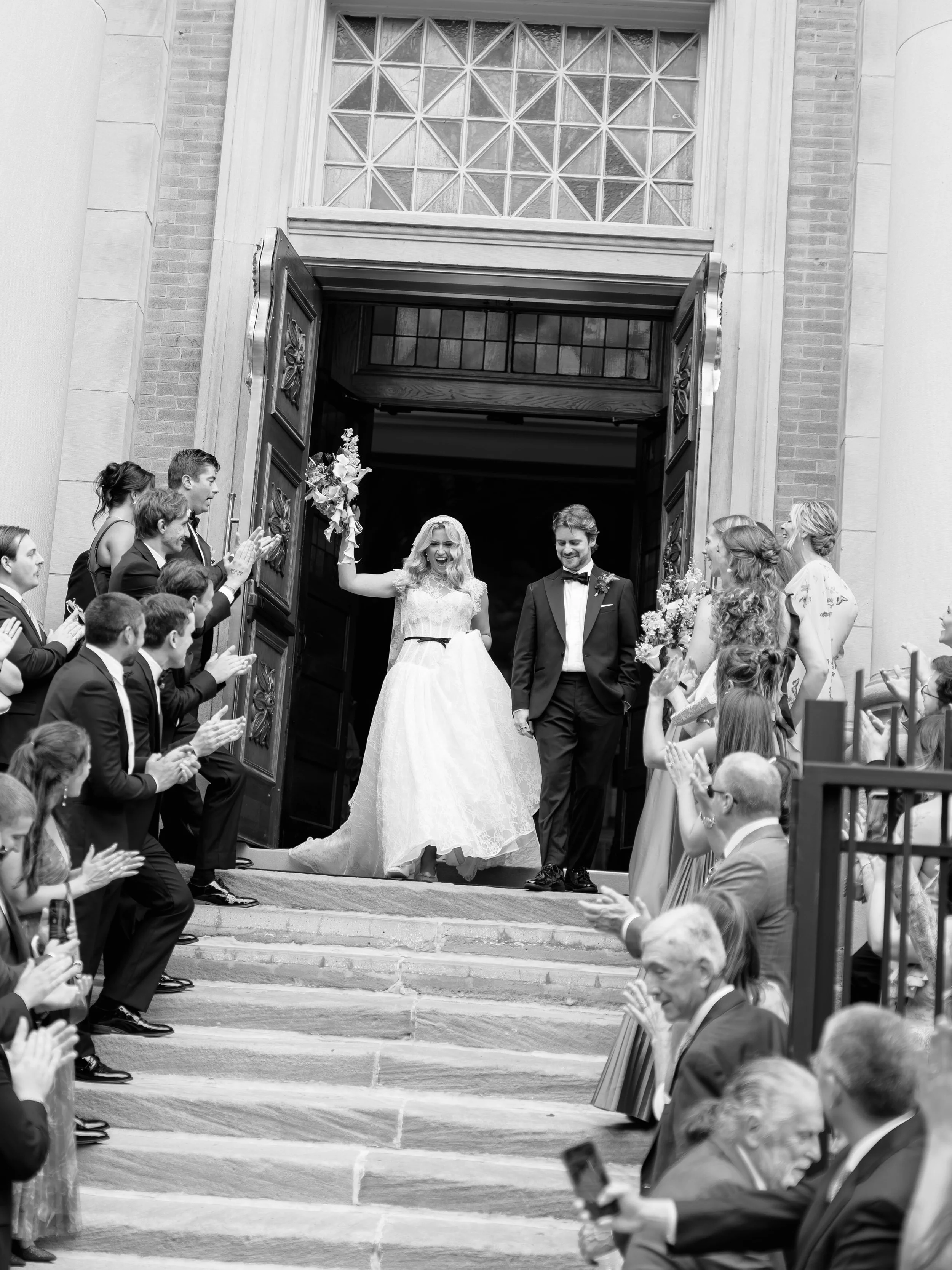 Black and white photo of the newlyweds exiting the church as guests cheer