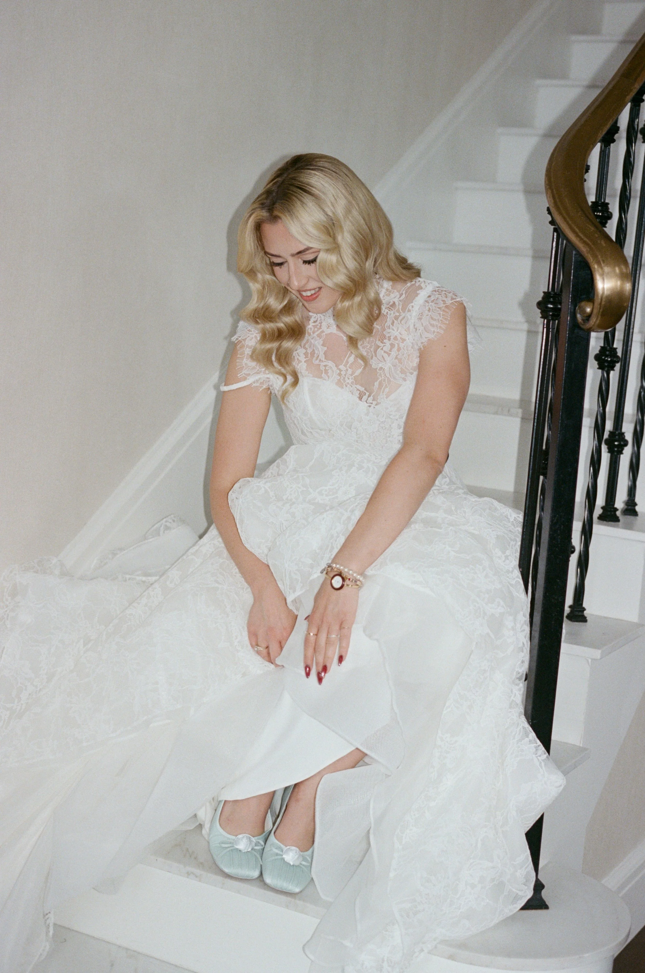 Bride sits on the staircase putting on her blue wedding heels