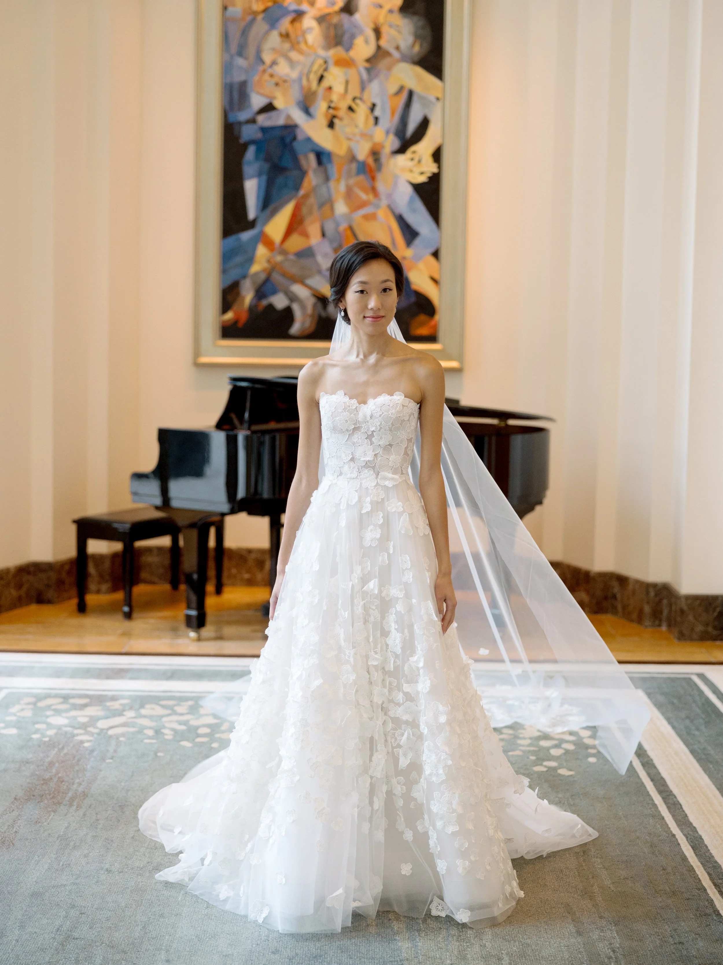 Full length film bridal portrait of the bride in a floral gown beside the grand piano in the Peninsula Chicago lobby