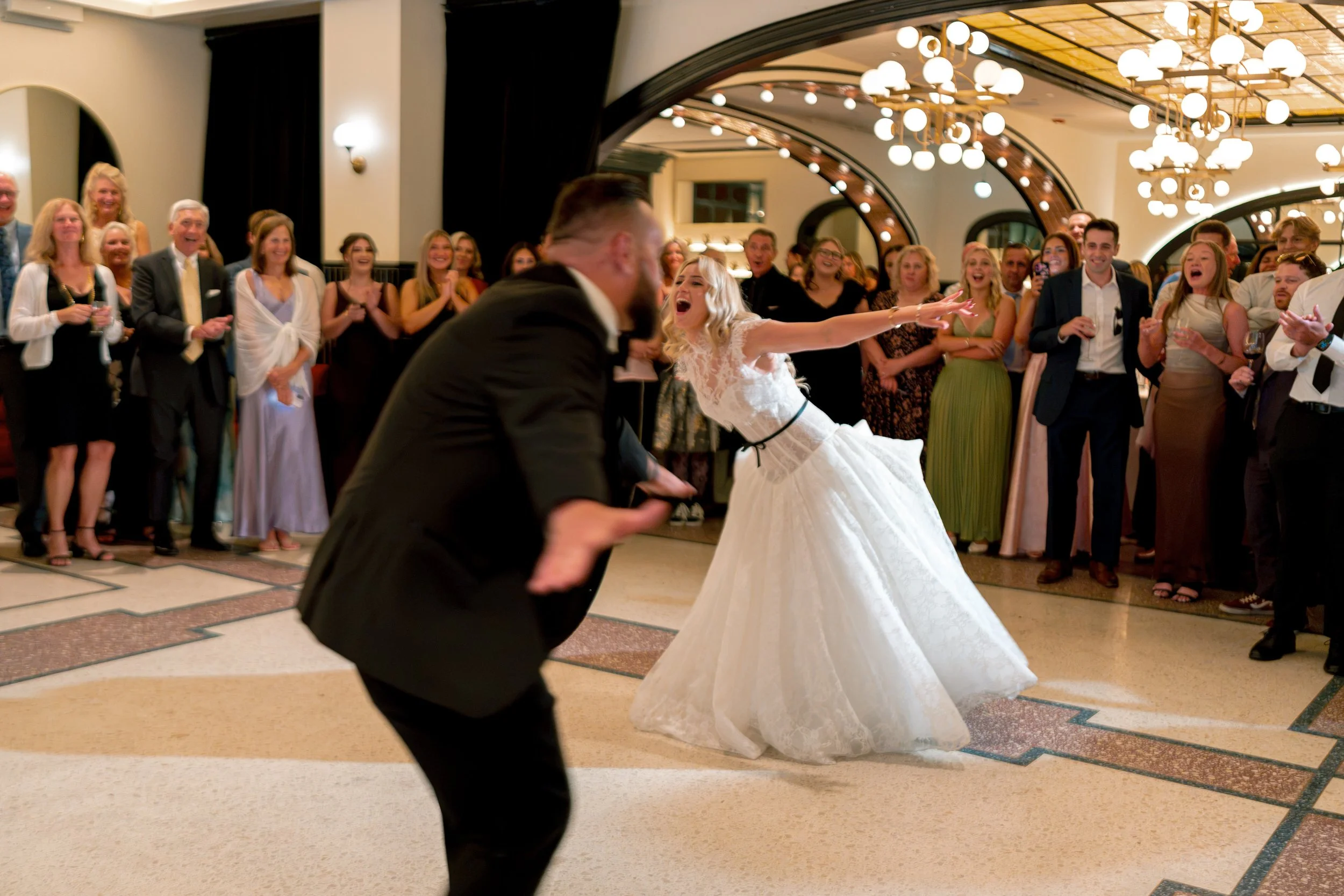 Newlyweds share their first dance as guests watch beneath glowing chandeliers