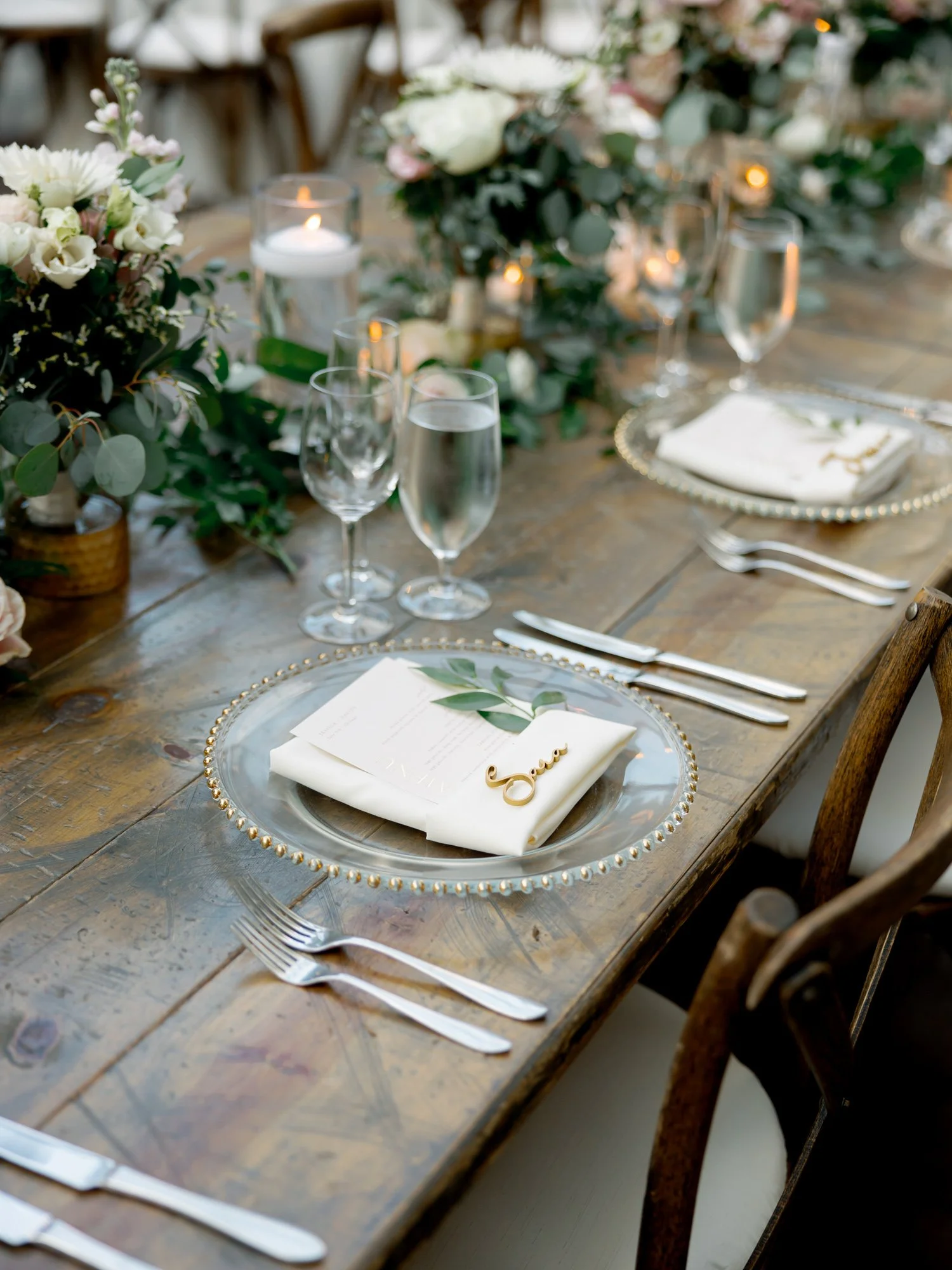 A rustic-elegant farm table place setting at the Chicago Illuminating Company, featuring a gold-beaded charger, fresh eucalyptus, and a scripted gold name card.