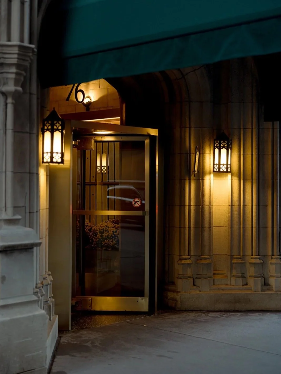 The University Club Chicago entrance at dusk — the gold revolving door glowing beneath a stone Gothic archway, lanterns casting warm light over the "76" address. A venue exterior detail that says everything about the evening ahead