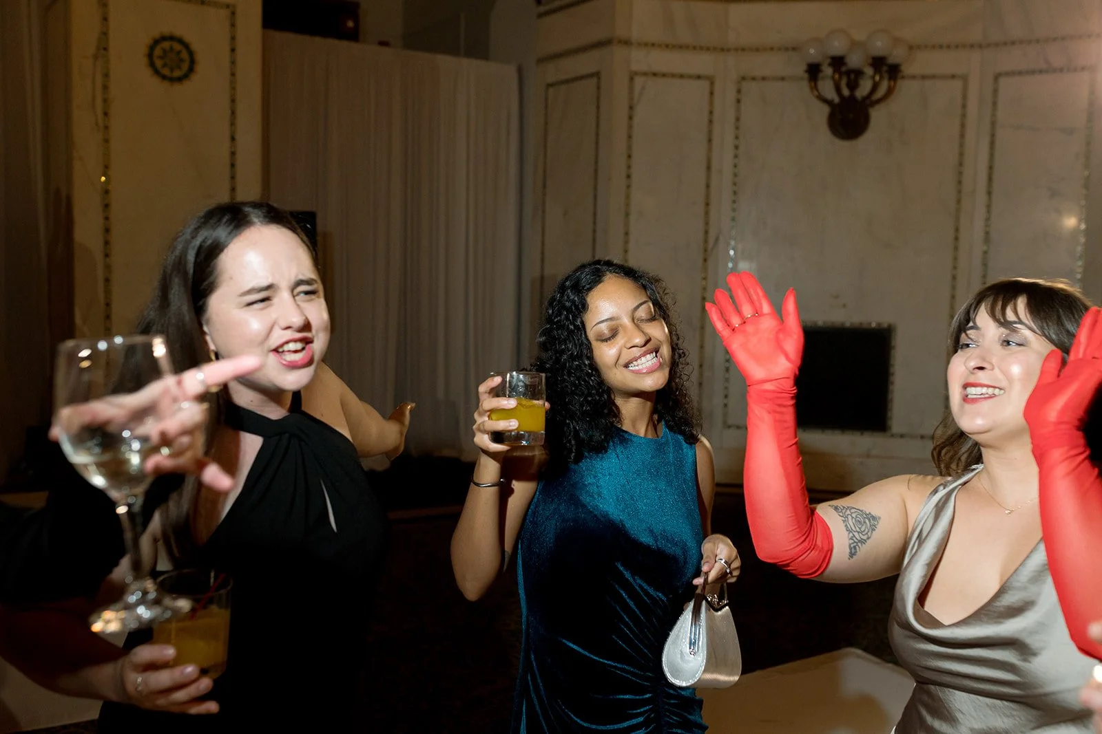 Female wedding guests celebrating together with cocktails during the reception, dressed in burgundy satin gowns. Shot on film by a Chicago wedding photographer.