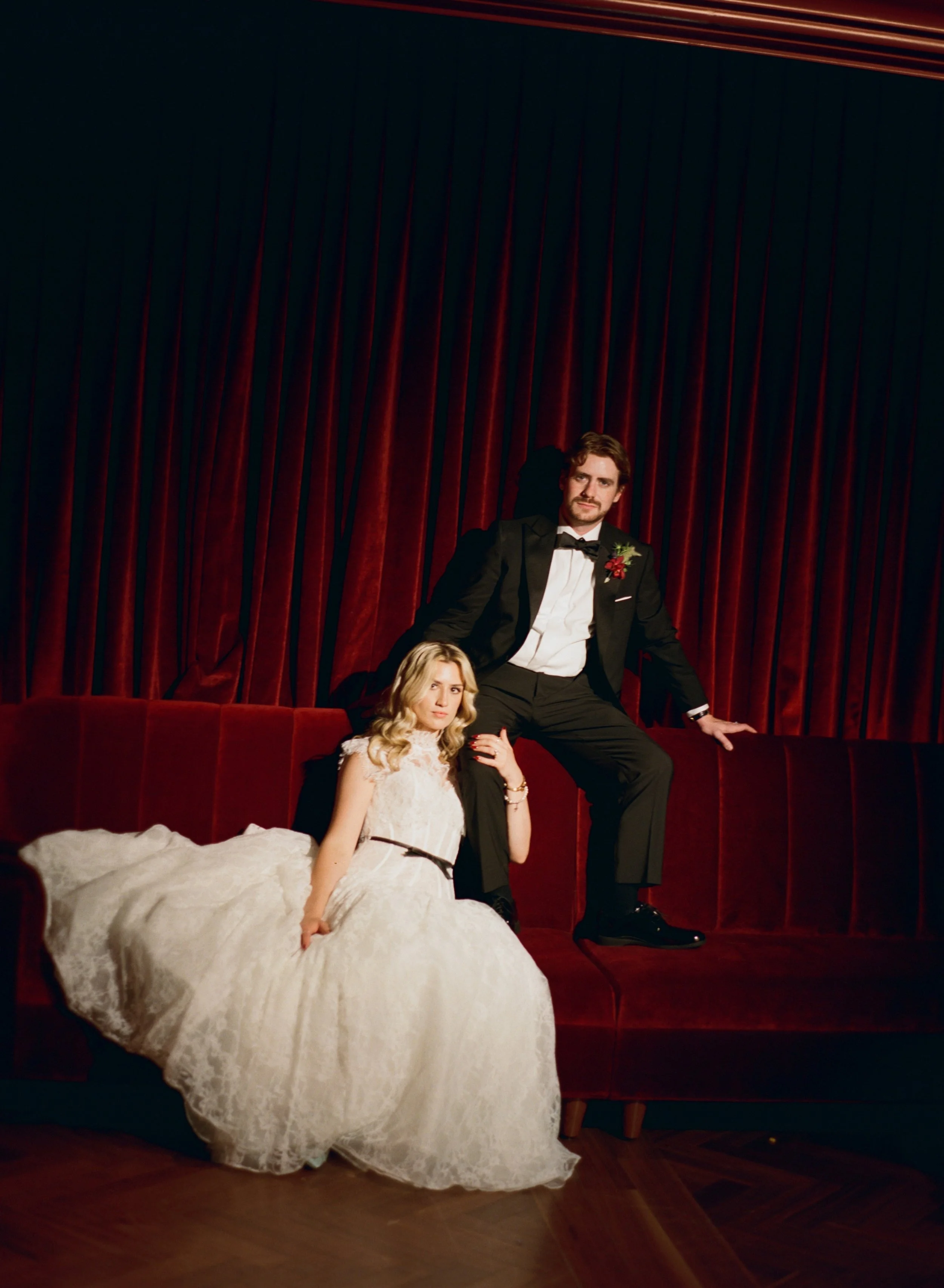 Bride and groom sit close together on the velvet couch in The Wellsley's red velvet lounge