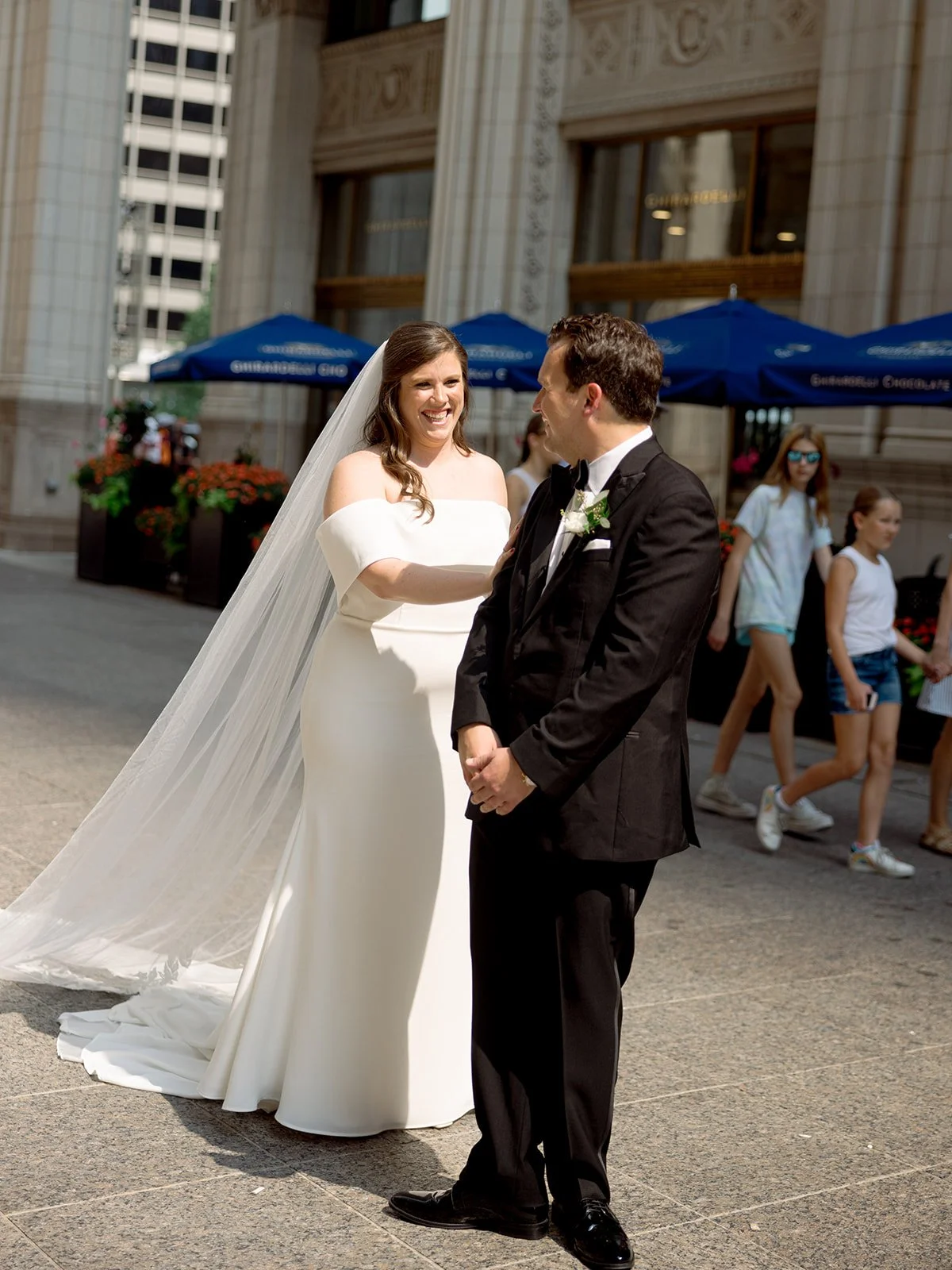 Bride and groom laughing in front of the Wrigley Building on Chicago's Magnificent Mile, cathedral veil in the summer breeze.