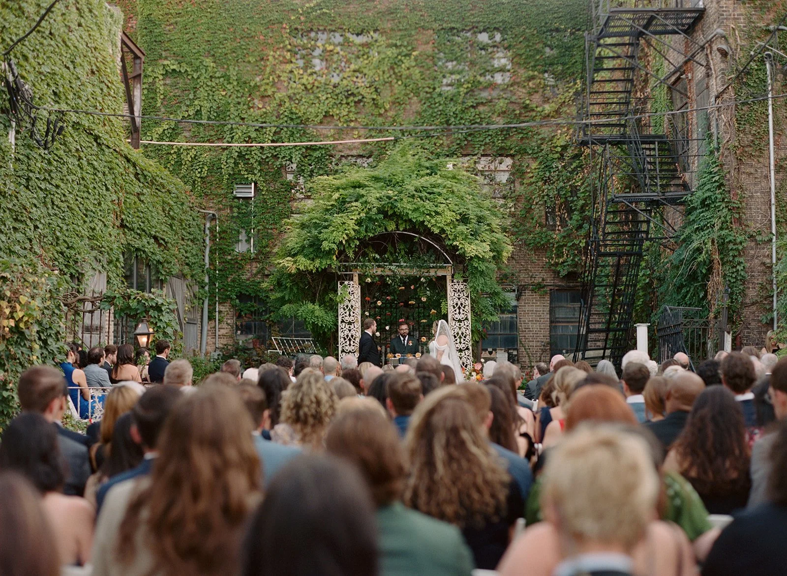 Medium format film wide shot of a wedding ceremony in the ivy-covered courtyard at Salvage One in Chicago, photographed by Chicago film wedding photographer Louie Abellera.