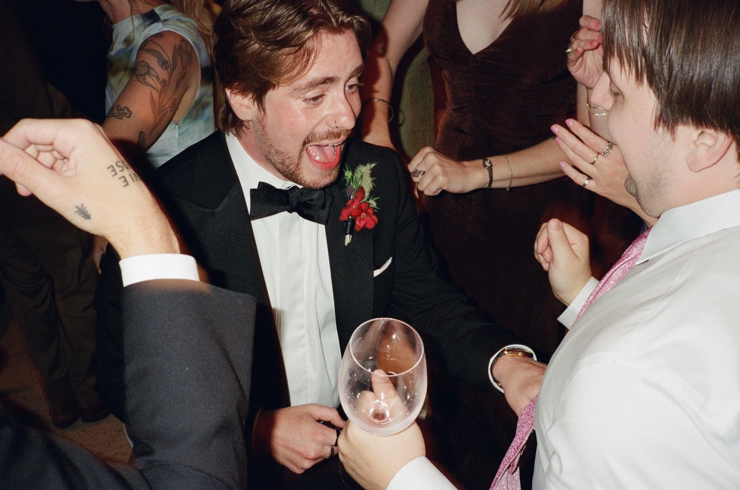 Groom laughs while holding a drink in a candid reception moment