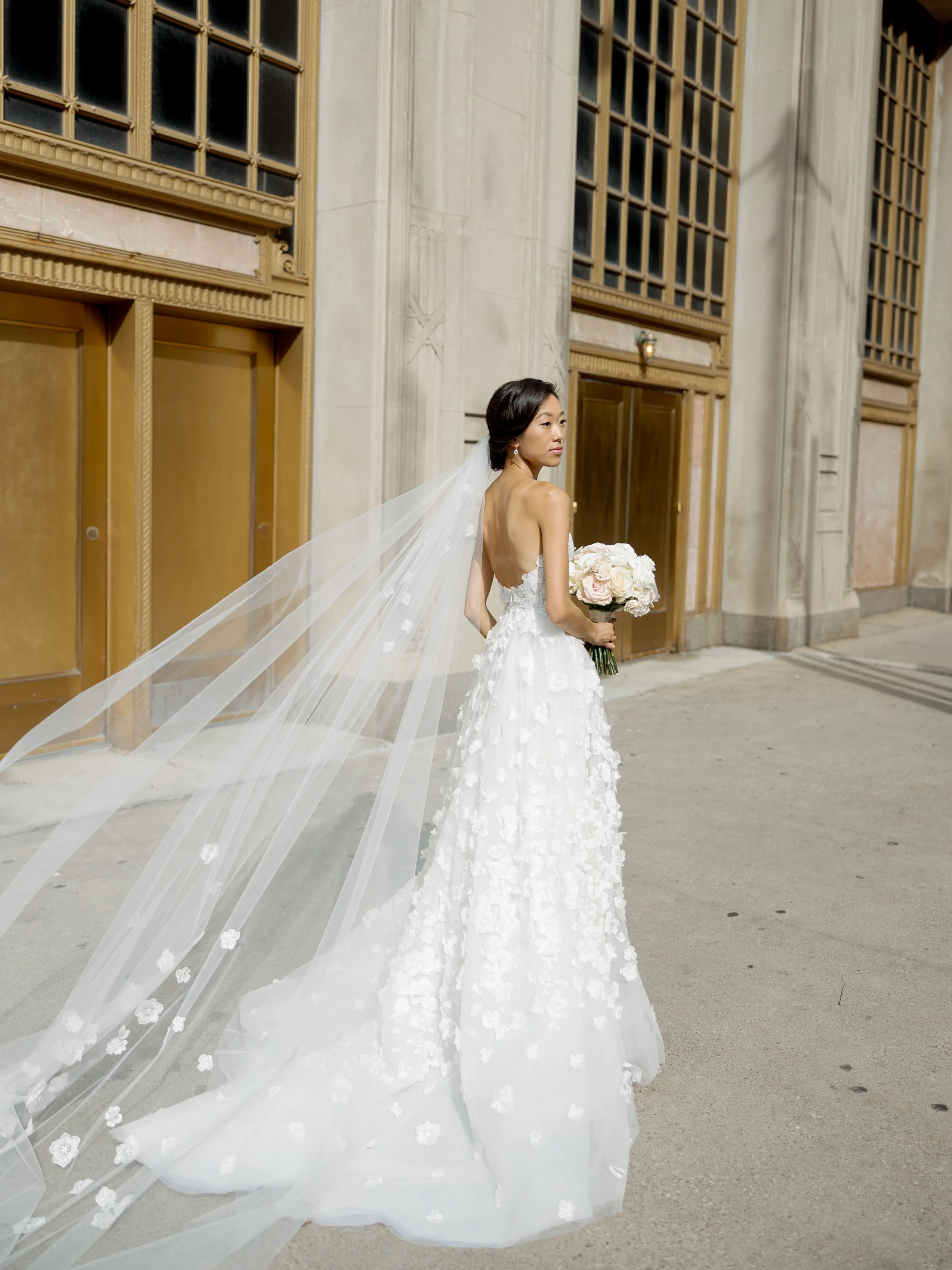 Back portrait of the bride in front of the Wrigley Building terra cotta doors, her long floral veil trailing behind