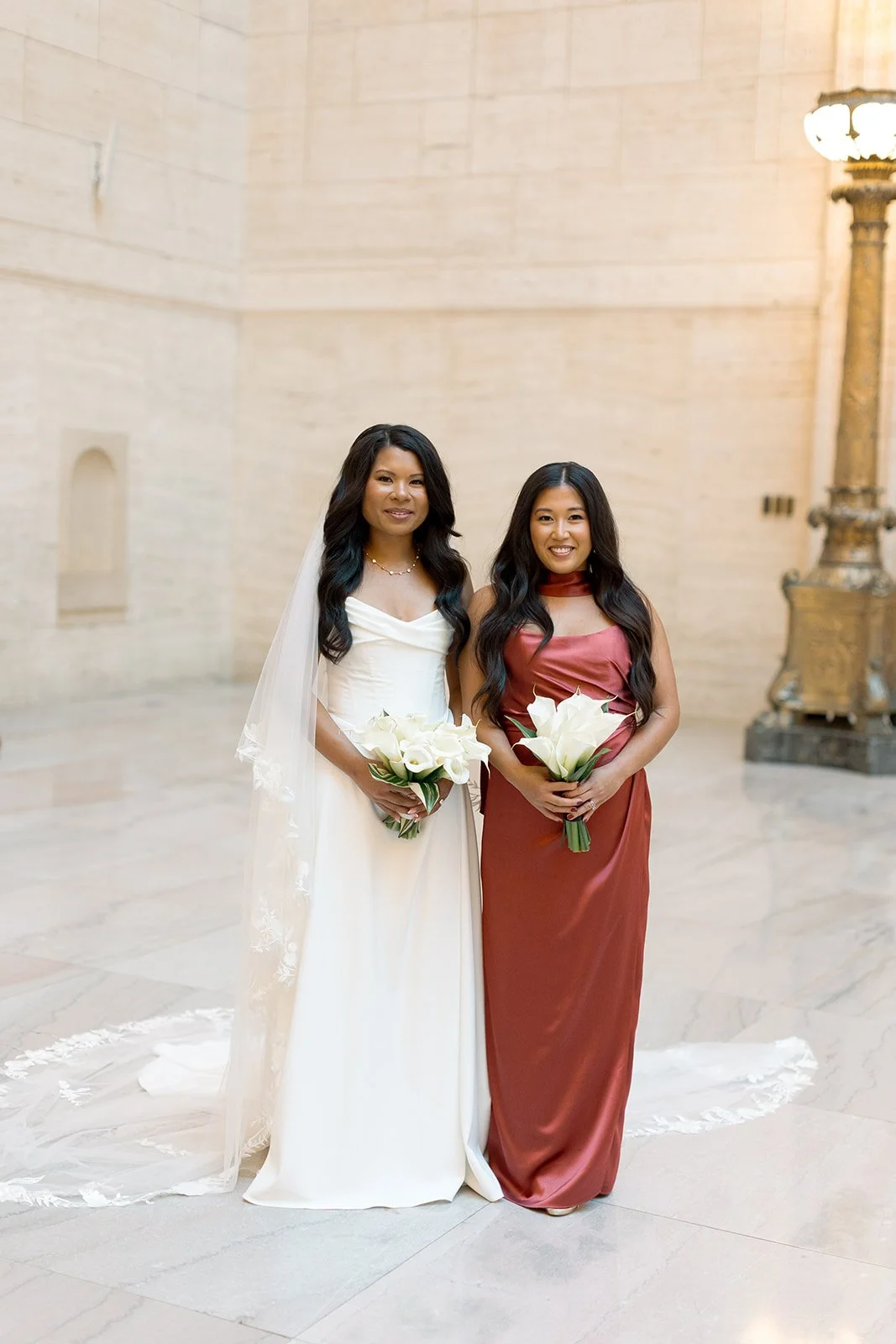 Sarah with a bridesmaid in the marble foyer of Union Station in Chicago, both holding white calla lily bouquets. Shot on film by a Chicago film wedding photographer.