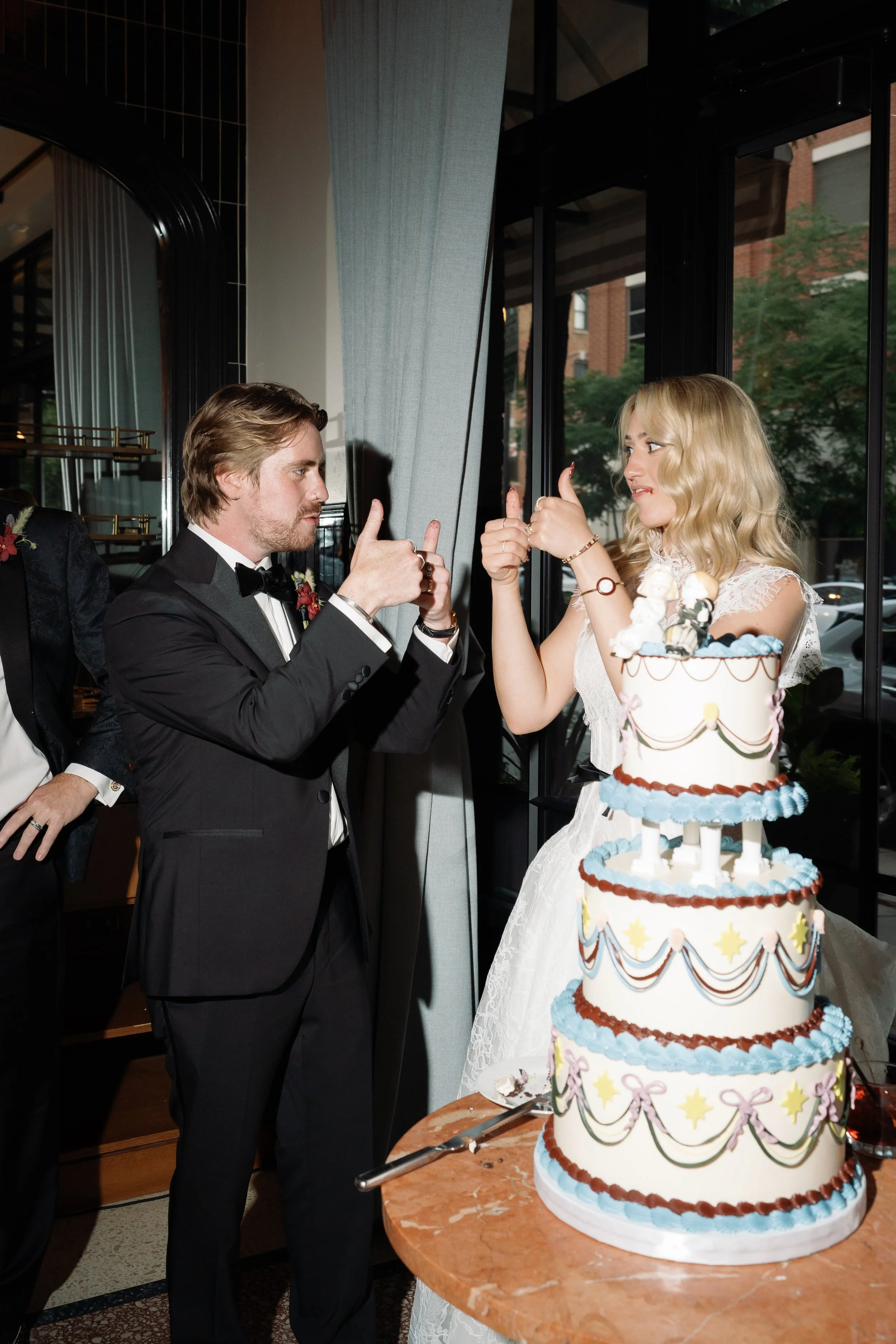 Bride and groom give a thumbs up while cutting their tiered wedding cake