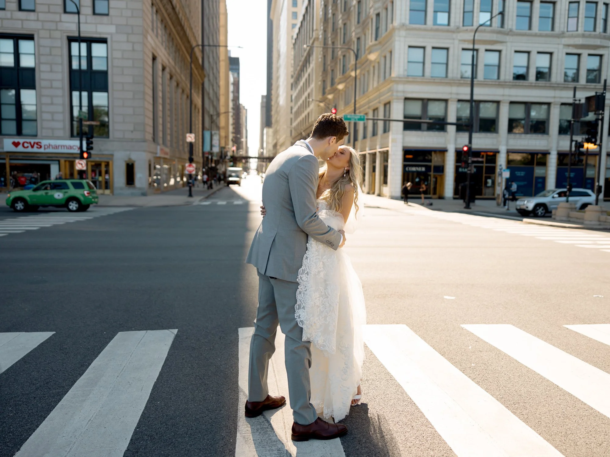 The bride and groom steal a cinematic kiss in the middle of a wide downtown Chicago intersection, the open city street stretching behind them in golden light.