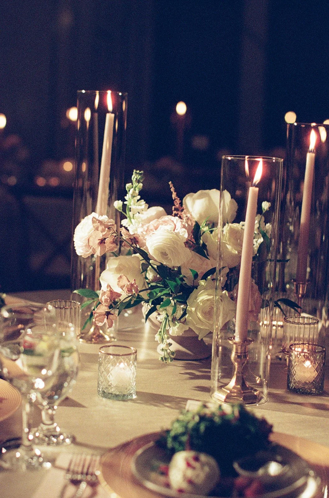 A lush floral centerpiece with white blooms, tall taper candles, and gold flatware on the reception table. Shot on film by a Chicago wedding photographer.