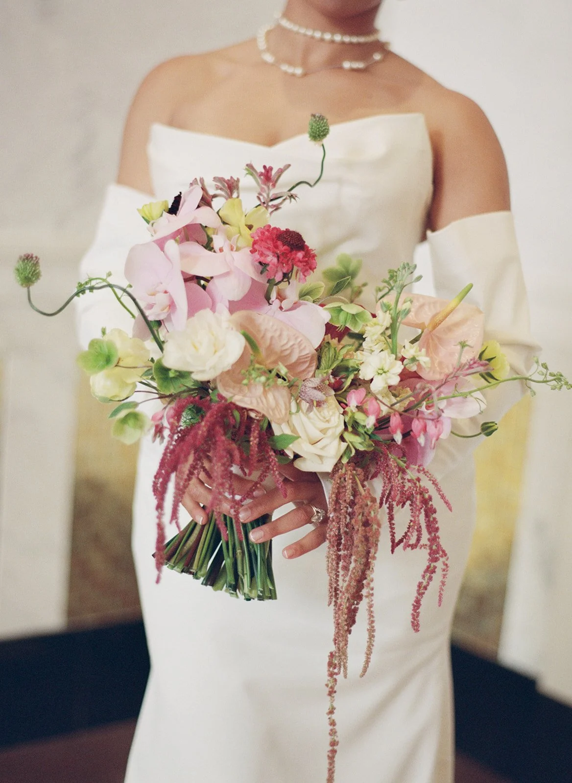 Medium format film detail of a bride holding a lush wildflower bouquet with orchids, anthurium, and trailing amaranth at the Old Post Office in Chicago, photographed by Louie Abellera.