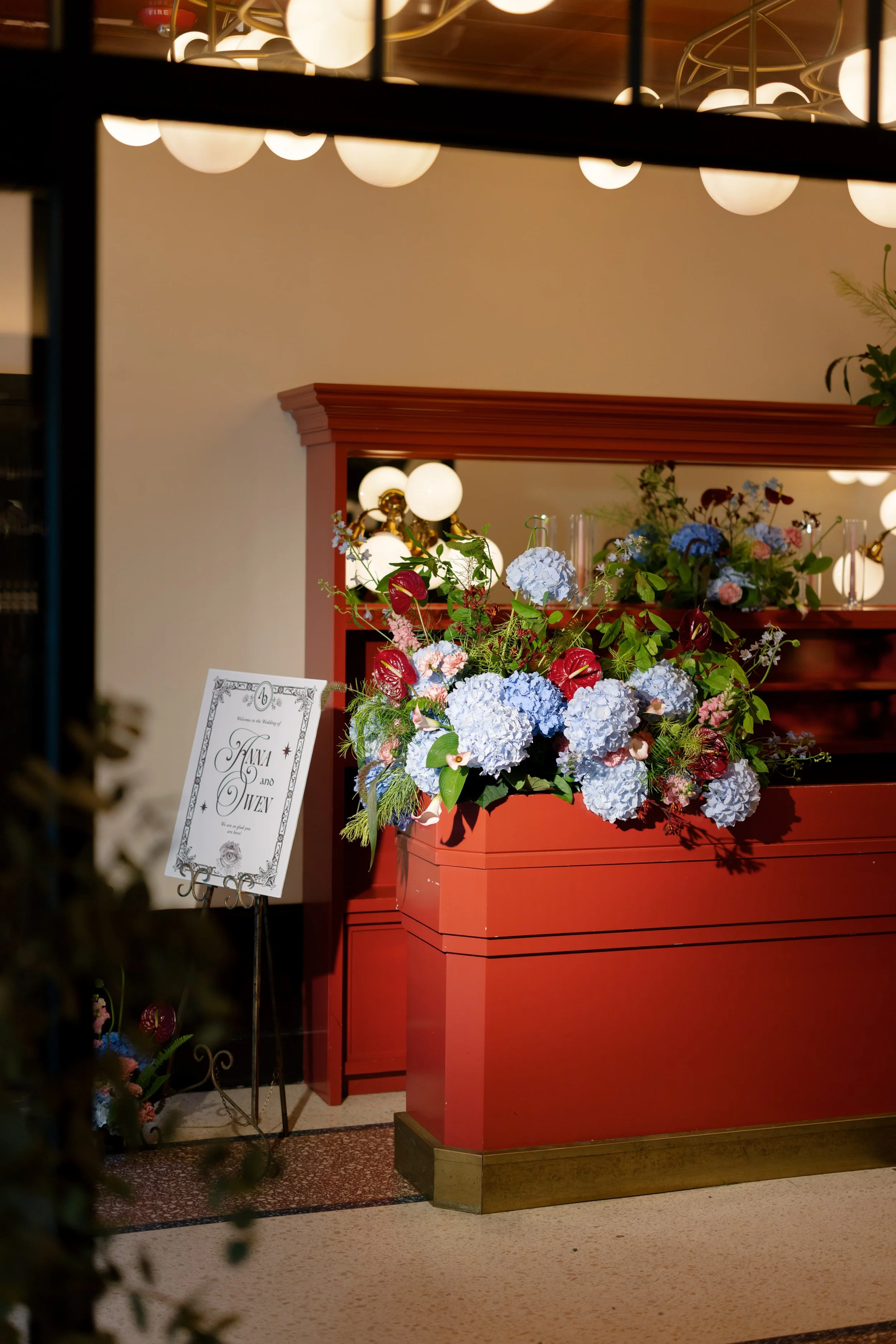 Floral arrangement styled on a red bar hutch beneath string lights