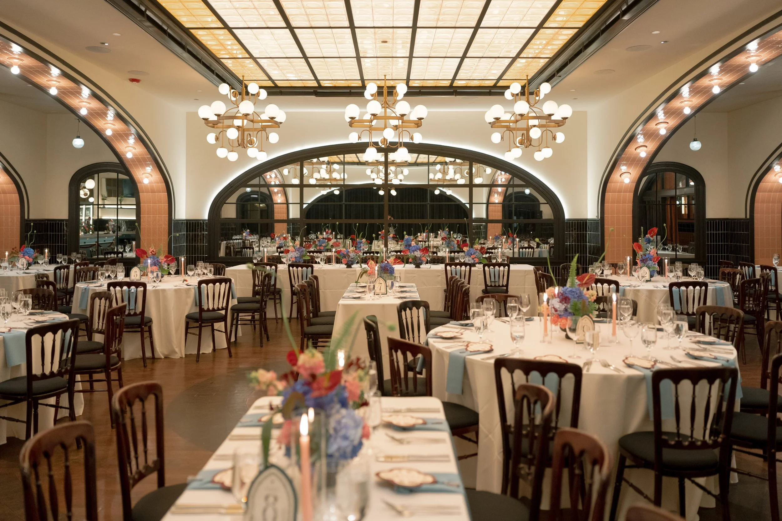 Wide shot of the reception dining room glowing beneath an arched skylight and chandeliers