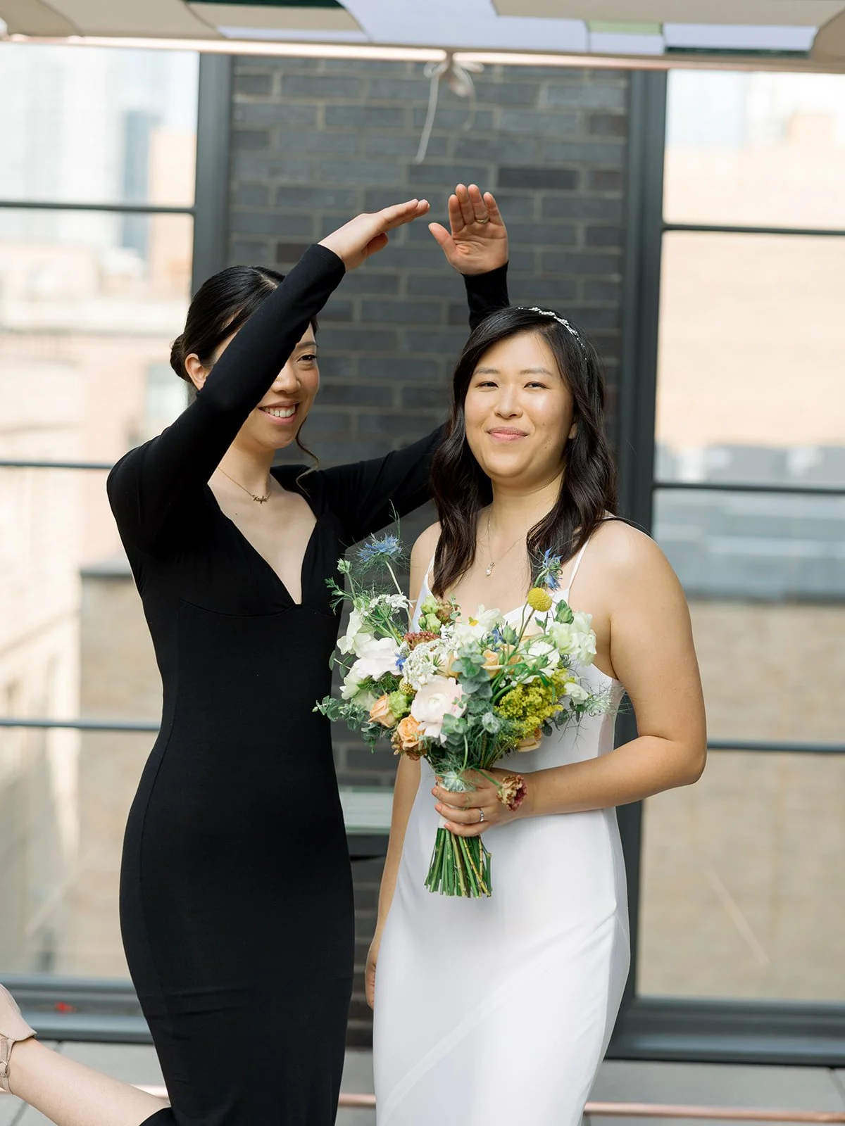 A bridesmaid in a sleek black dress spins the bride in front of a floor-to-ceiling window at The Hoxton Chicago — bouquet in hand, joy in her face. The kind of pre-ceremony moment that sets the whole tone for the day.
